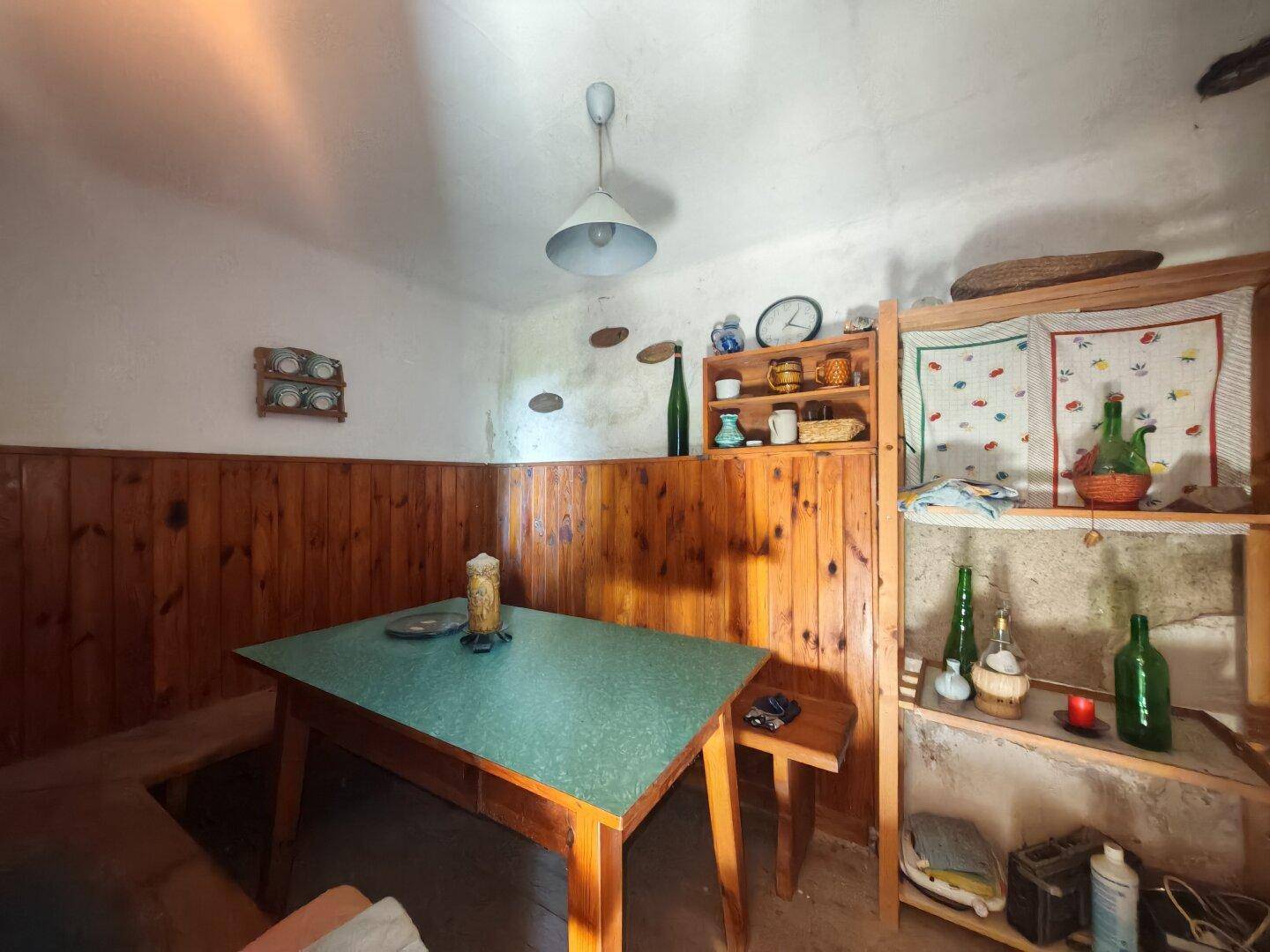 Gemütlicher, rustikaler Essbereich mit Holzvertäfelung, einem einfachen Tisch und Regalen mit Dekorationen.