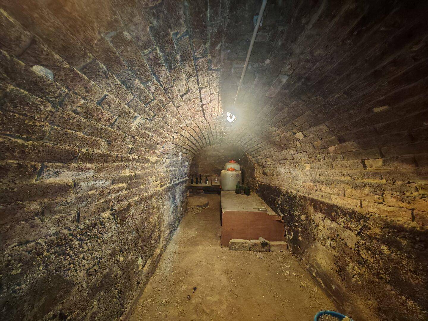 Langer, schmaler Gewölbekeller aus Ziegelsteinen mit einer einzelnen Lichtquelle.