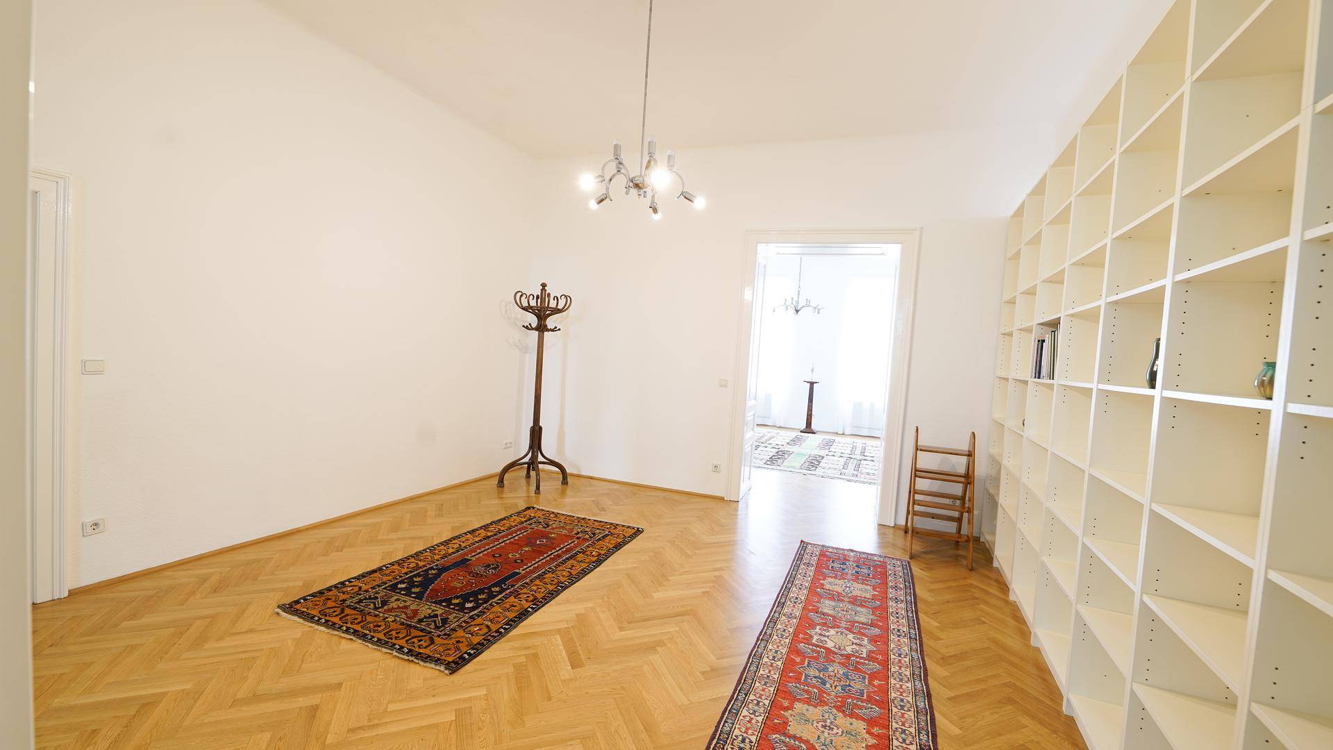 Heller Eingangsbereich mit Fischgrätparkett, Teppichen, Garderobe und einer großen Bücherwand.