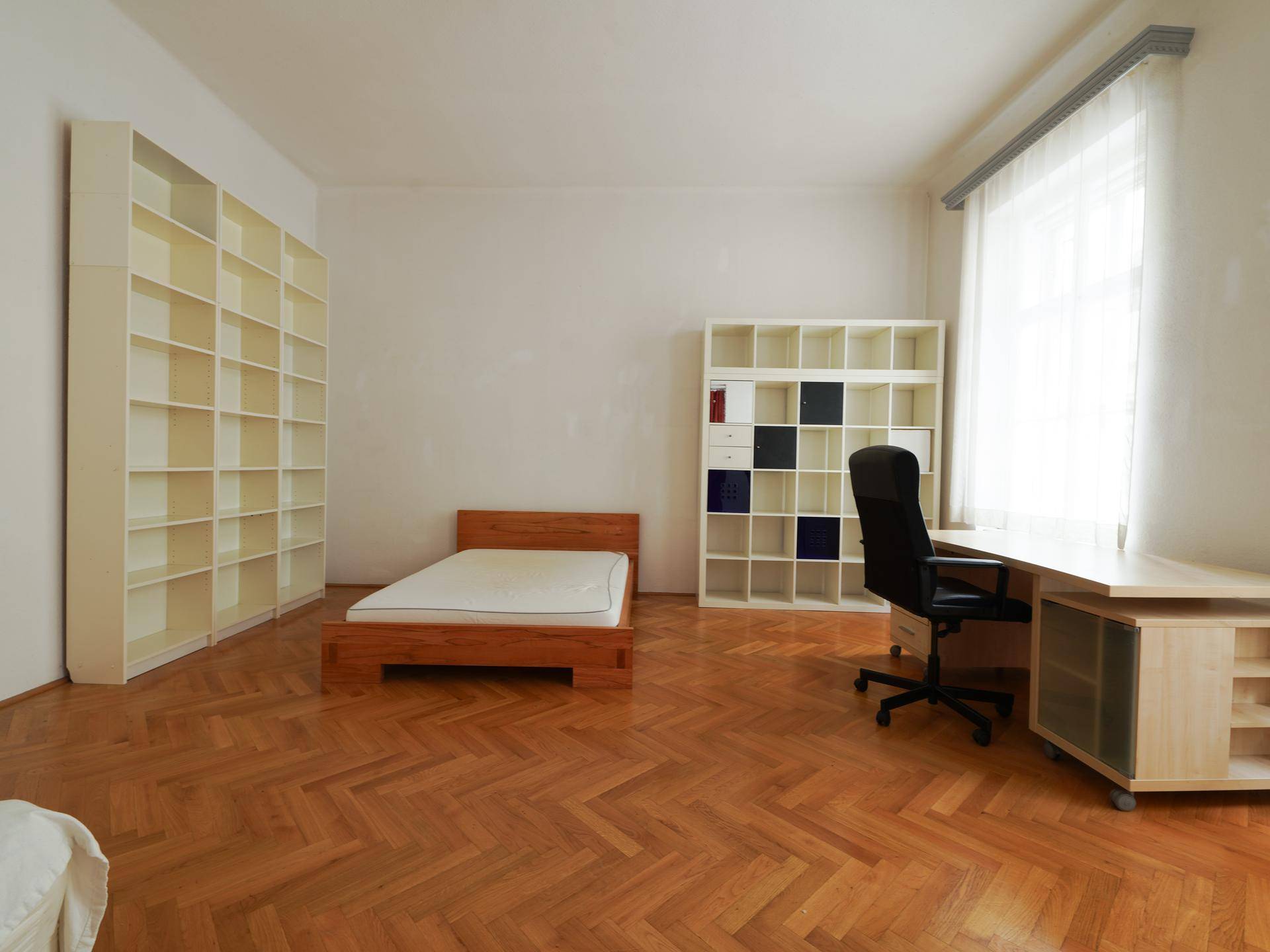 Helles Schlafzimmer mit Holzbett, Schreibtisch und großen Bücherregalen auf Fischgrätparkett.