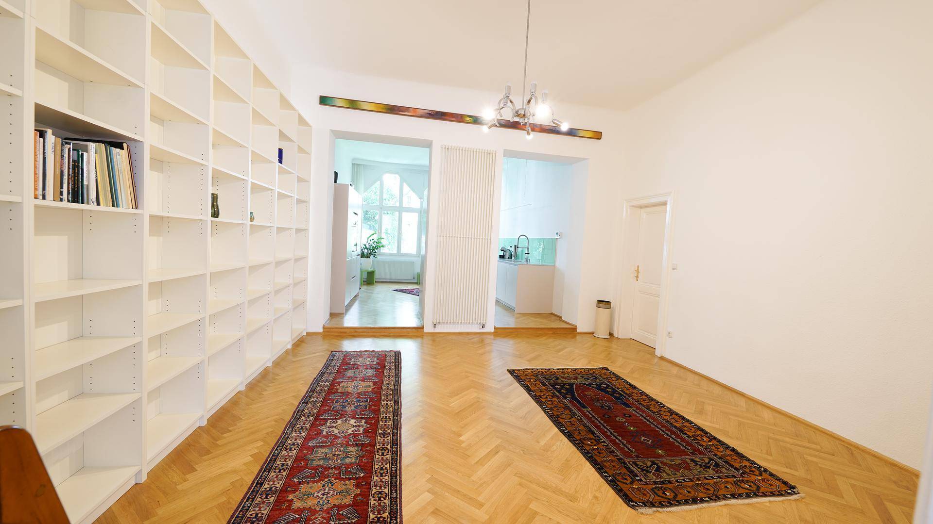 Geräumiges Wohnzimmer mit raumhohen Bücherregalen, zwei Teppichen und elegantem Fischgrätparkett.