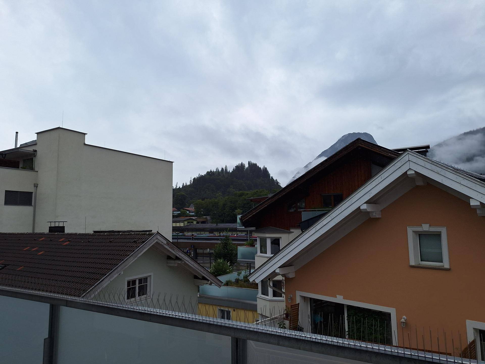 Blick auf umliegende Häuser und bewaldete Berge unter einem bewölkten Himmel, der eine weite Aussicht bietet.