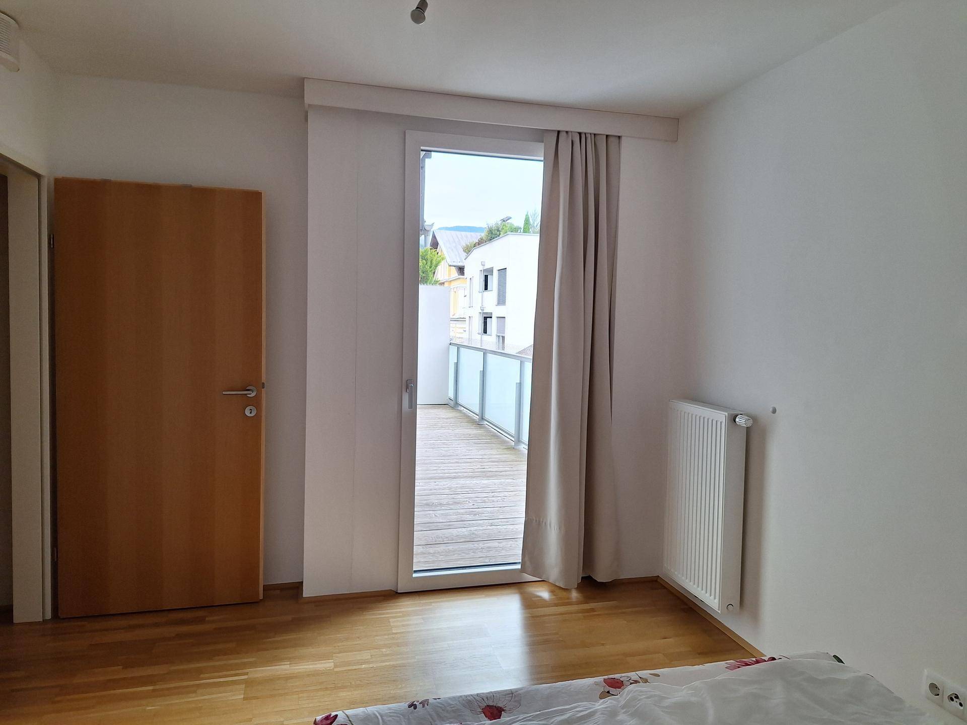 Schlafzimmer mit Holzboden und einer großen Balkontür, die viel natürliches Licht hereinlässt.