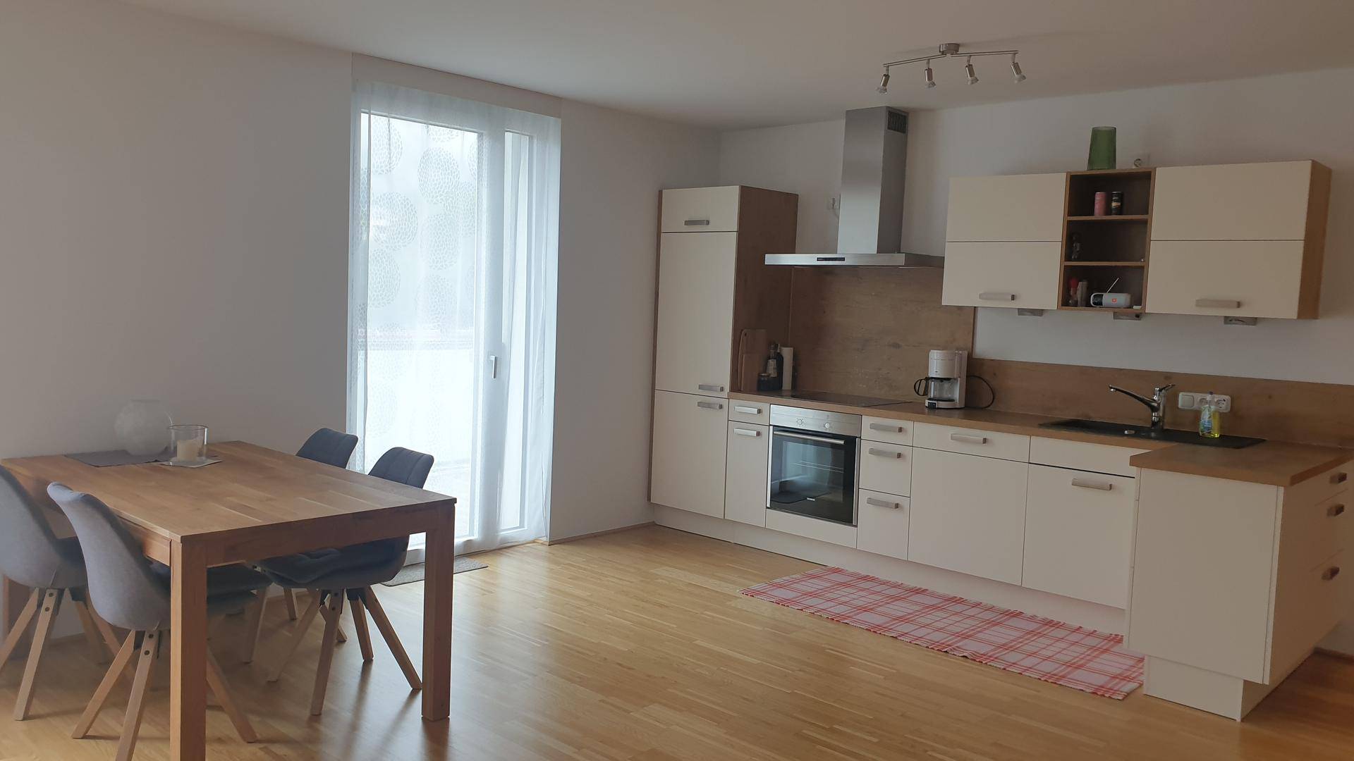 Offener Wohn-Essbereich mit moderner Küche, Holztisch und Stühlen sowie Zugang zu einem Balkon.