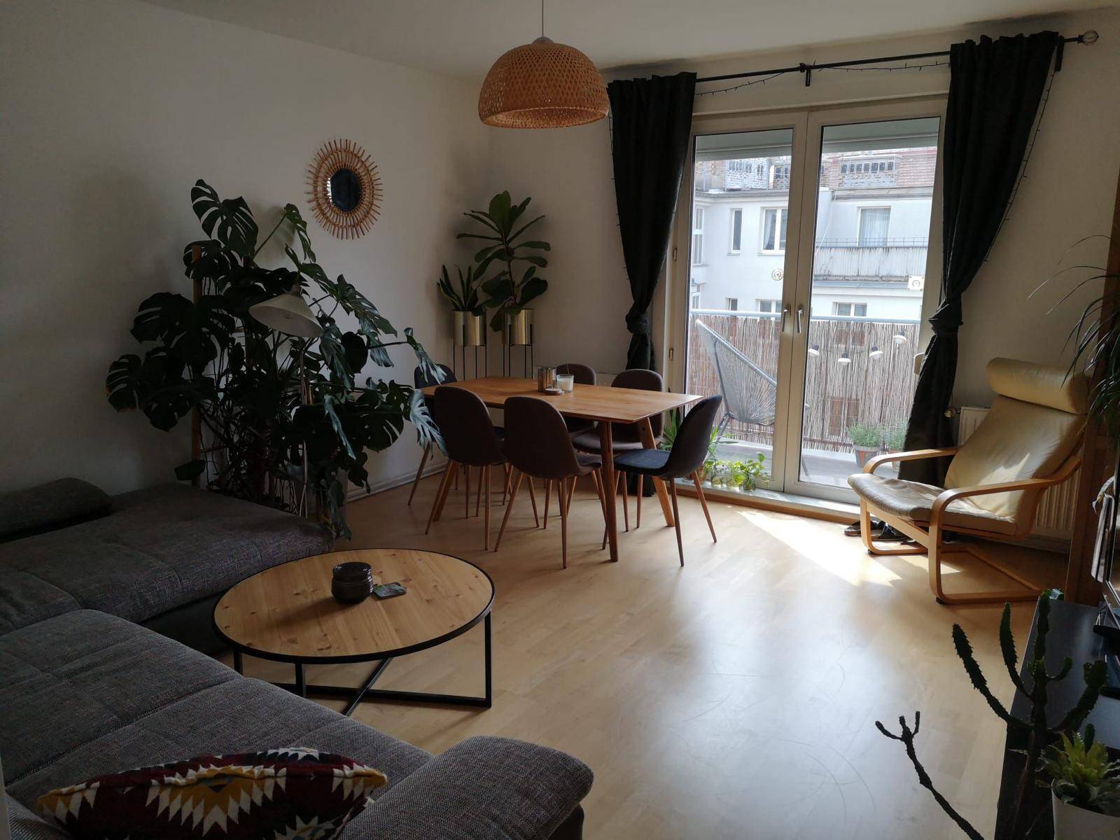 Heller Wohn-Essbereich mit Sofa, Esstisch und Zugang zum Balkon, dekoriert mit Pflanzen.