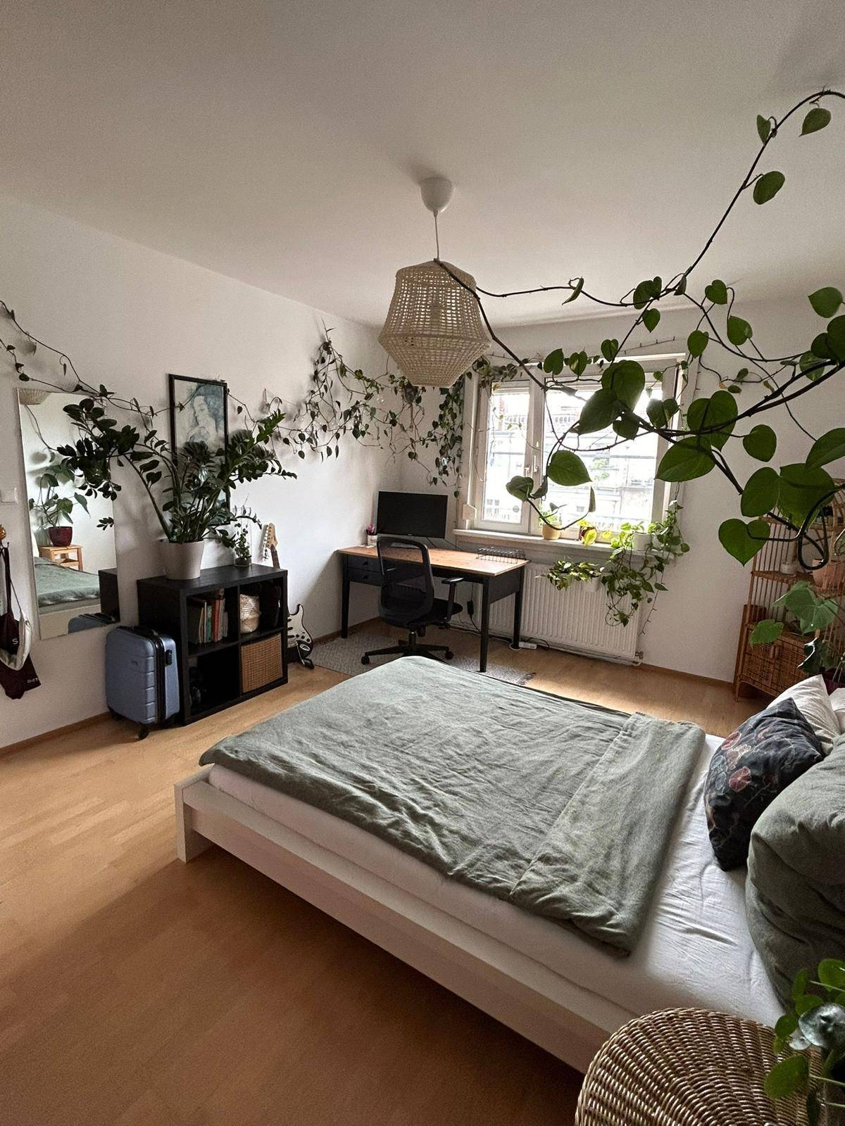 Helles Schlafzimmer mit Holzboden, Schreibtisch und üppiger grüner Pflanzendekoration.