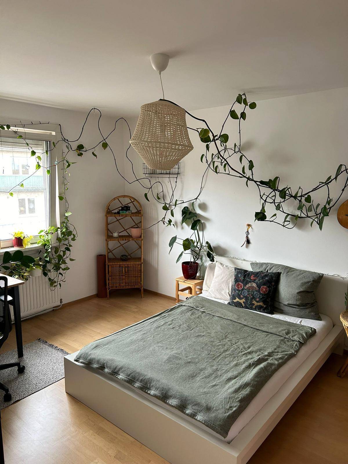 Gemütliches Schlafzimmer mit Holzboden, Rattanlampe und vielen Pflanzen, die eine natürliche Atmosphäre schaffen.
