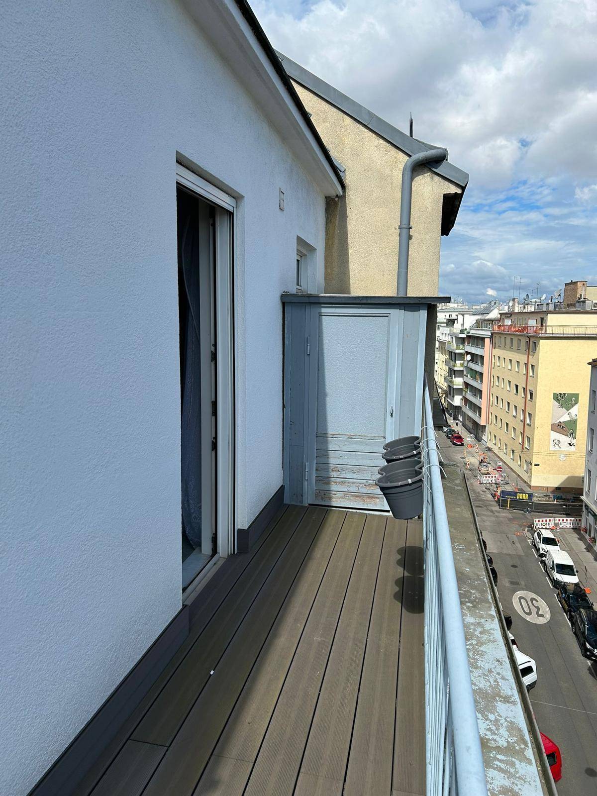 Langer, schmaler Balkon mit Holzdielen und Blick auf die darunterliegende Straße und Stadtlandschaft.
