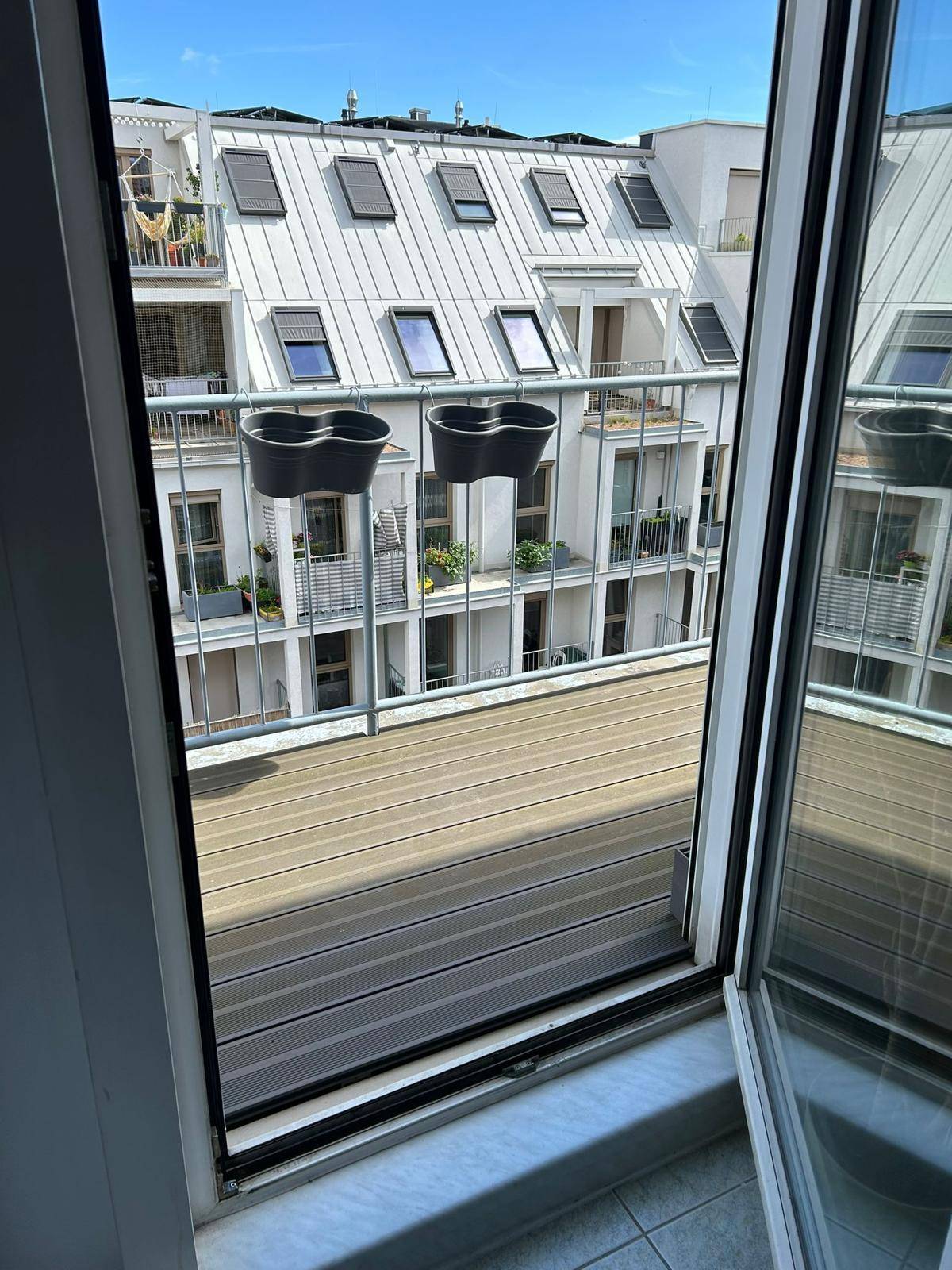 Blick von innen durch die offene Balkontür auf den Balkon und die gegenüberliegende Gebäudefassade.
