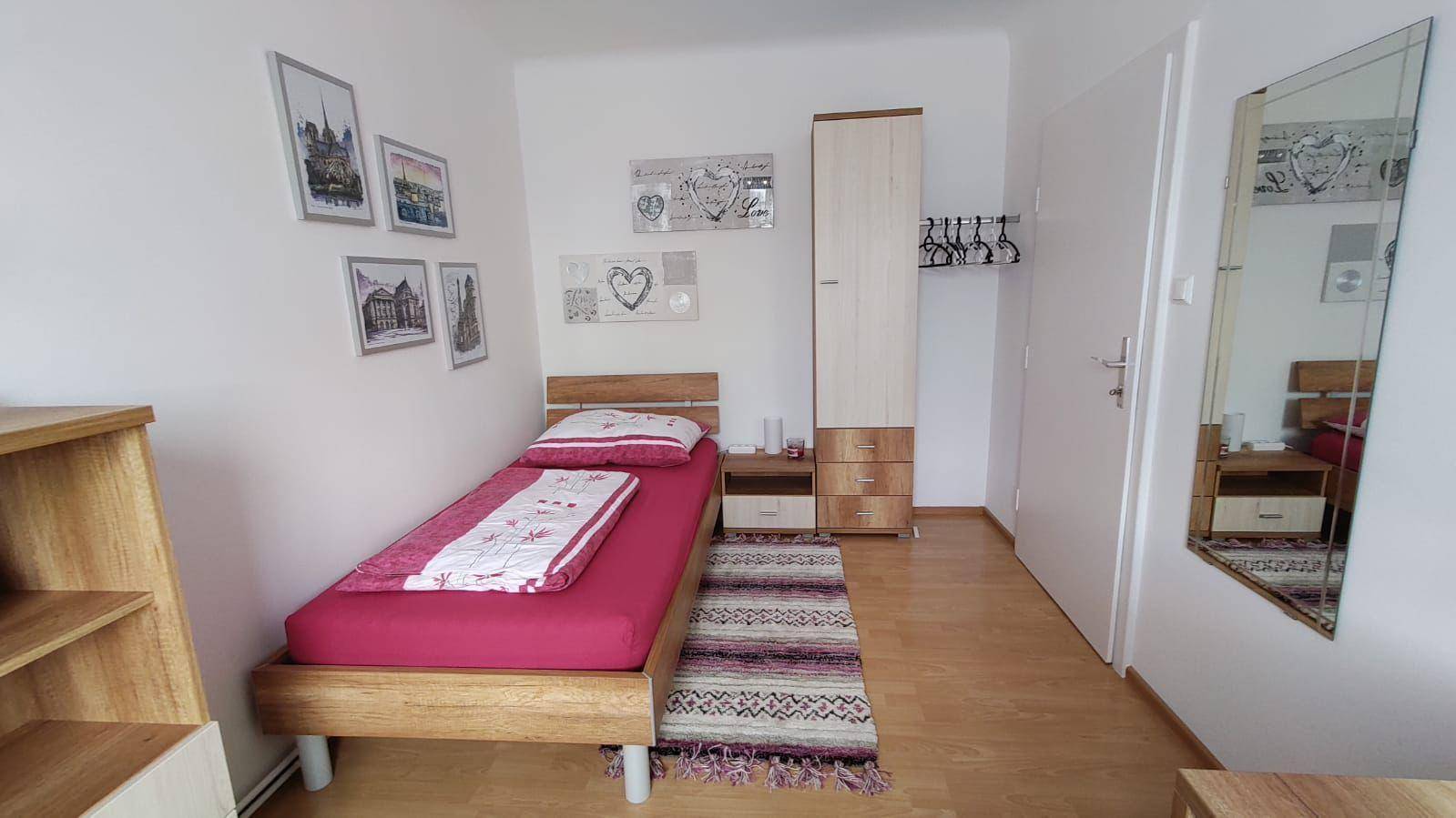 Kleines Schlafzimmer mit Einzelbett, hellem Holzmobiliar und einem großen Wandspiegel.
