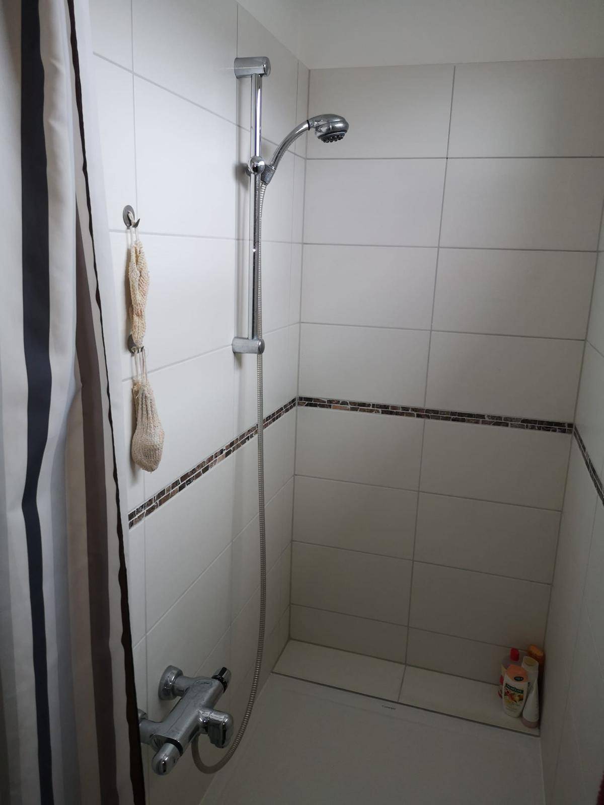 Duschbereich im Badezimmer mit weißen Fliesen und einer einfachen Duschvorrichtung.