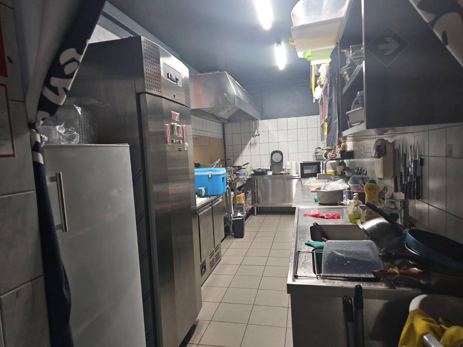 Professionelle Gewerbeküche mit Edelstahloberflächen, großen Kühlschränken und Dunstabzugshaube für den Betrieb.