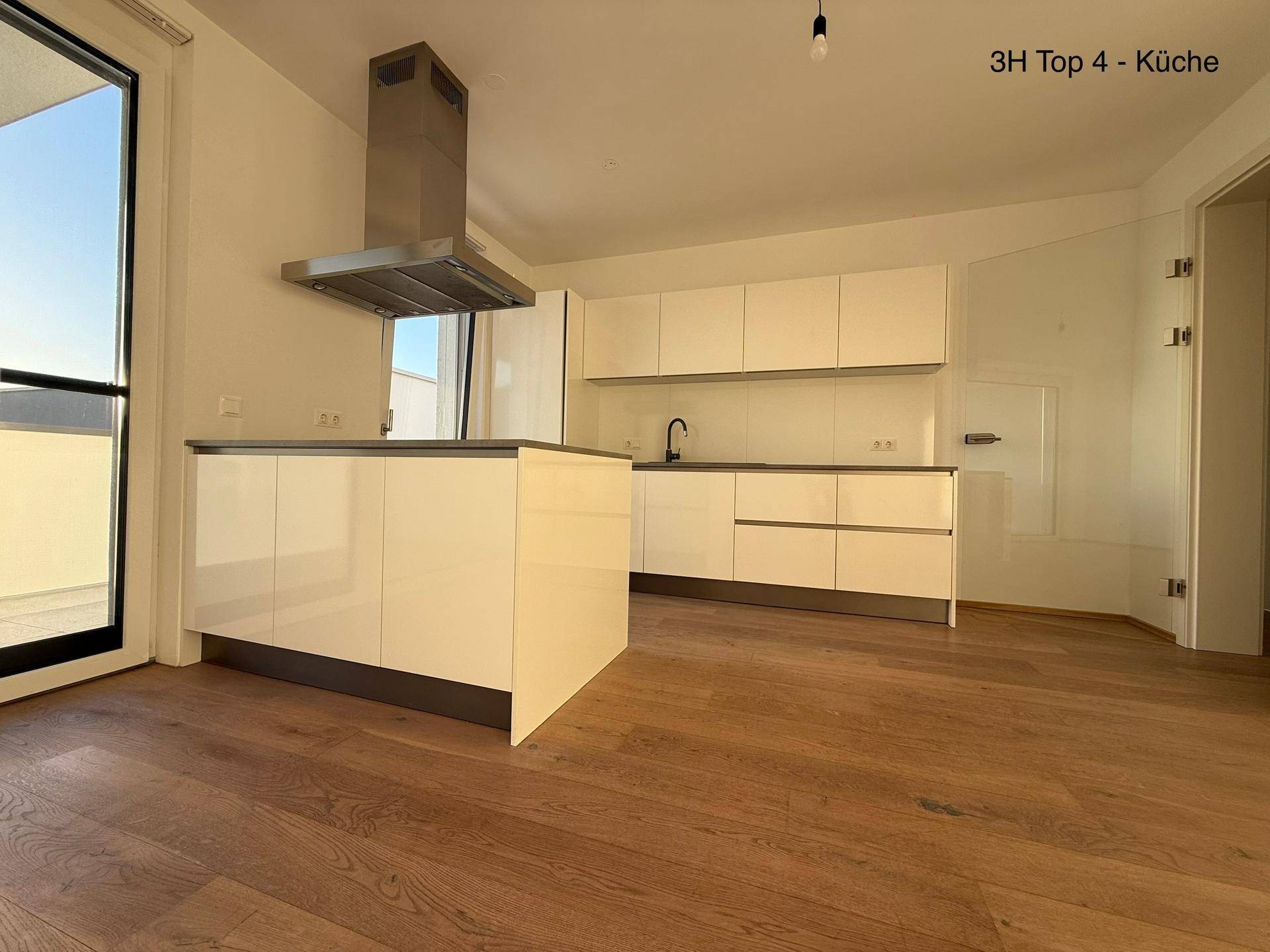 Moderne Küche mit weißen Hochglanzfronten, Kücheninsel und Holzboden, mit Zugang zum Balkon.