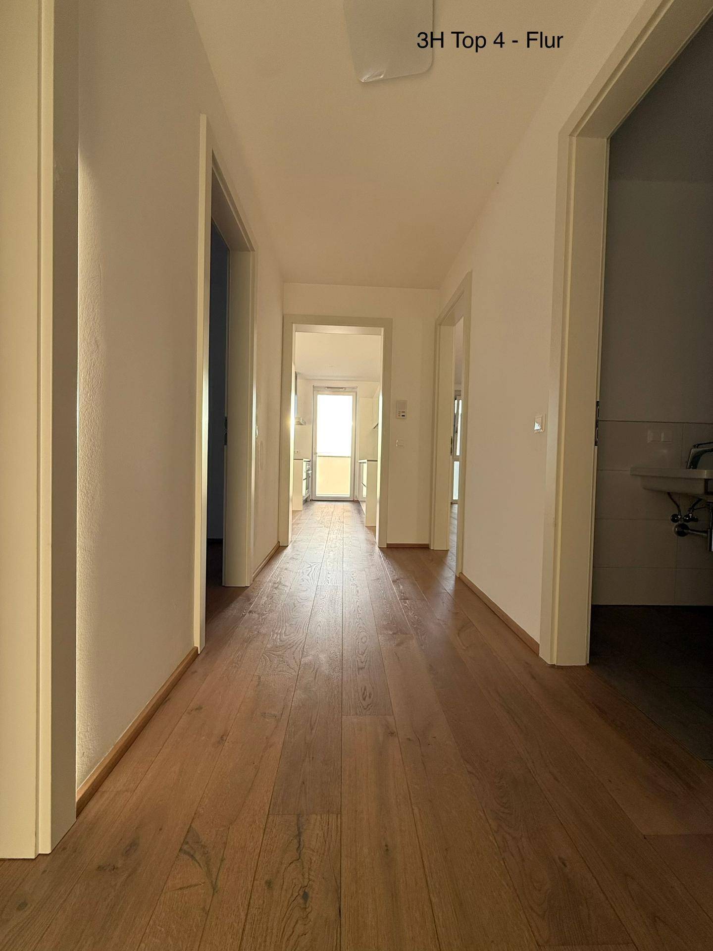 Heller Flur mit warmem Holzboden, der zu verschiedenen Zimmern und einem hellen Ende führt.