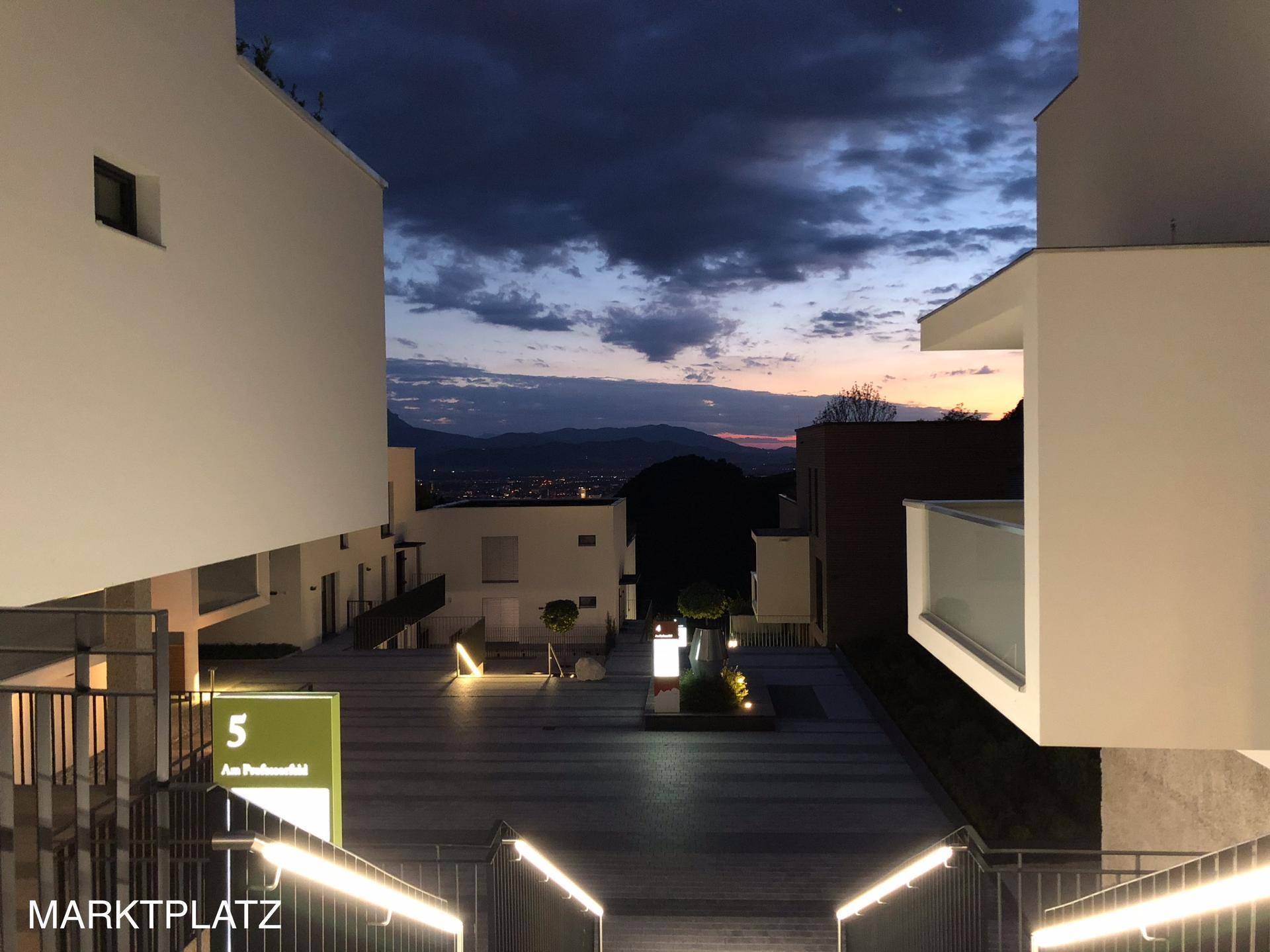 Moderner Innenhof bei Sonnenuntergang mit beleuchteten Wegen und Blick auf die Stadt.