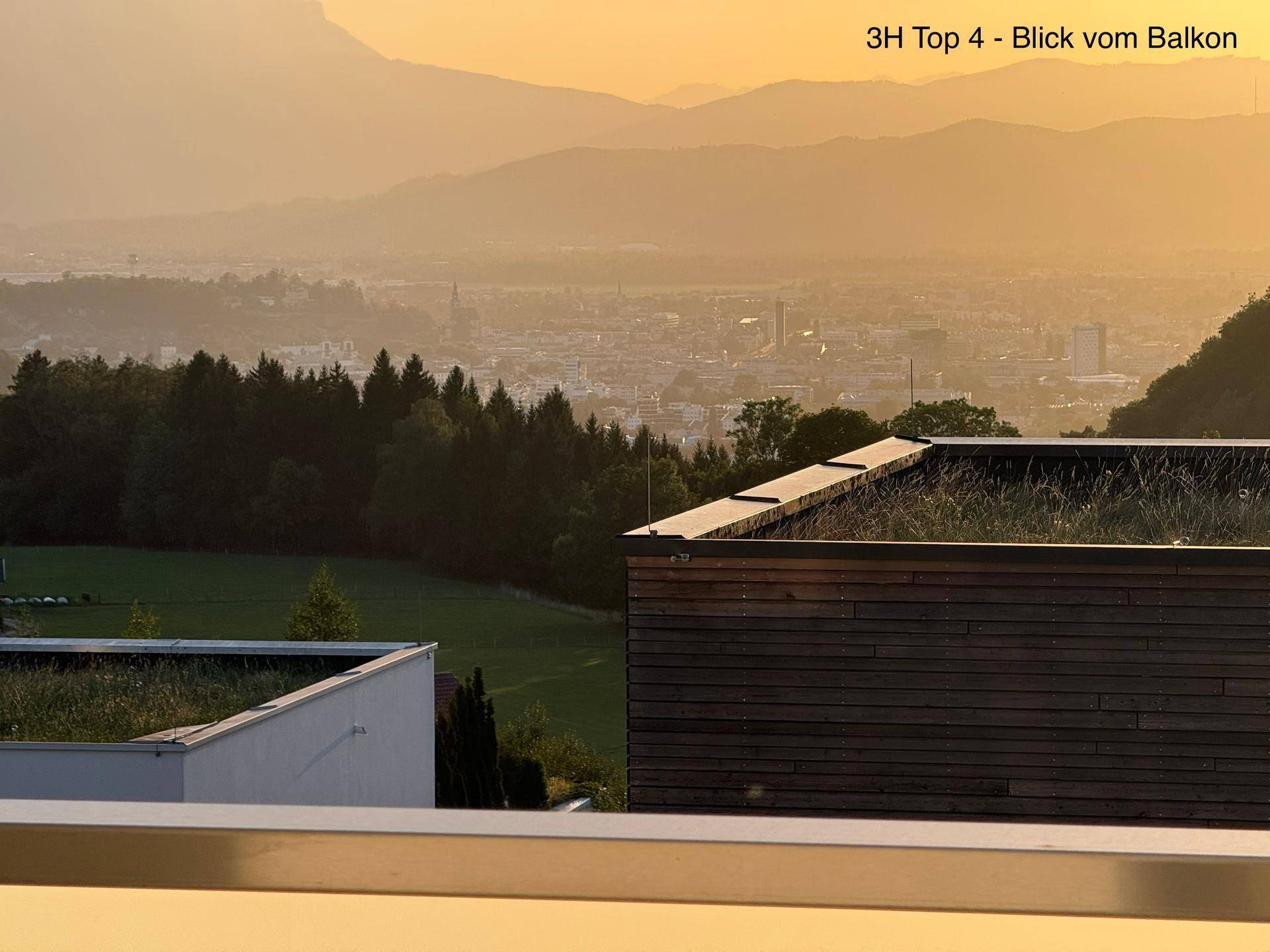 Weitläufiger Blick vom Balkon auf eine Stadt in der Ferne, grüne Hügel und moderne Dächer.