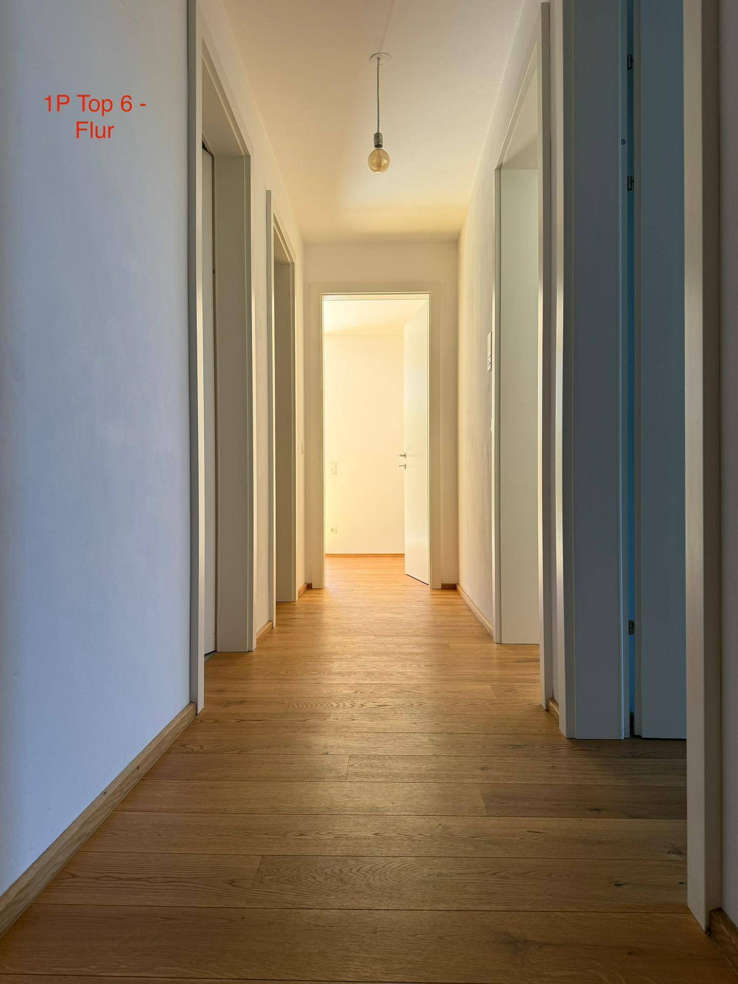 Heller Flur mit Eichenparkettboden, weißen Wänden und Zugang zu verschiedenen Zimmern.