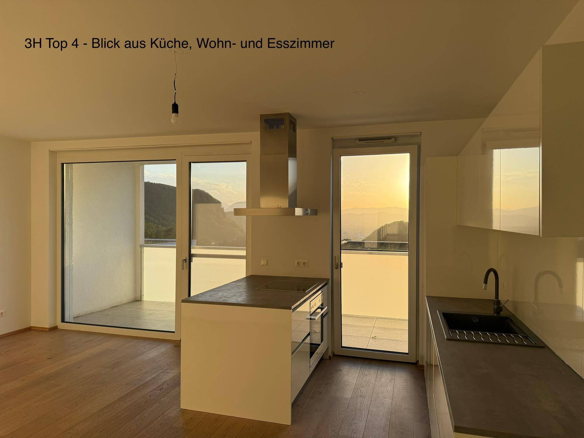 Offener Wohn-Essbereich mit moderner Küche, Kücheninsel und großem Balkonzugang mit Sonnenuntergangsblick.