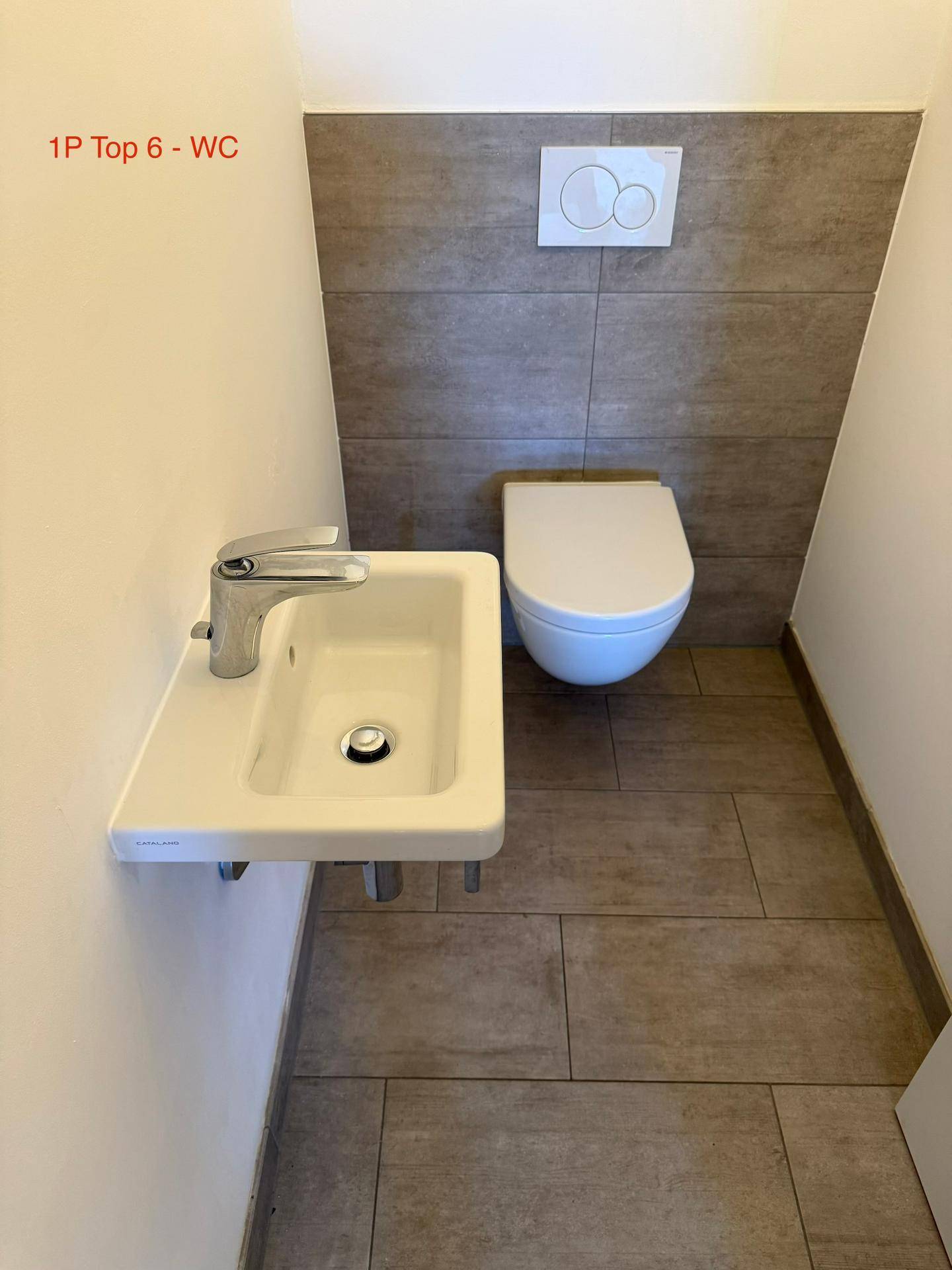 Modernes Gäste-WC mit Wand-WC, kleinem Waschbecken und grauen großformatigen Fliesen.