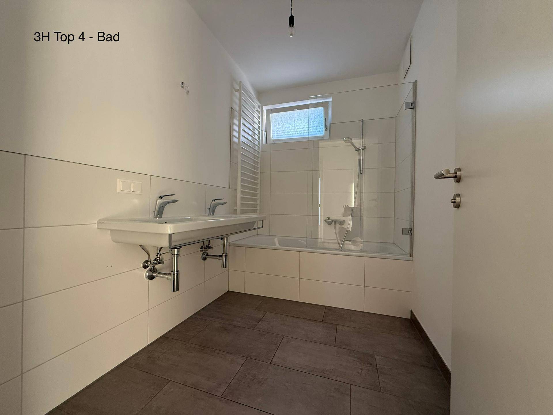 Modernes Badezimmer mit Badewanne, Duschwand, Doppelwaschbecken und beheiztem Handtuchhalter.