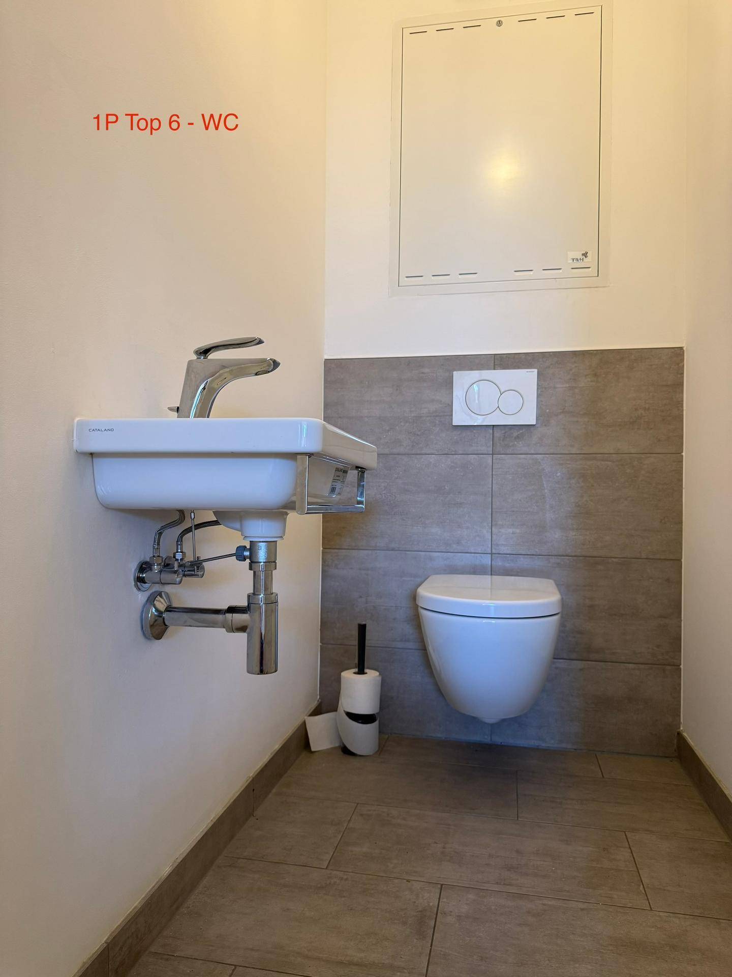 Funktionales Gäste-WC mit Wand-WC, kleinem Waschbecken und praktischer Wandverkleidung.