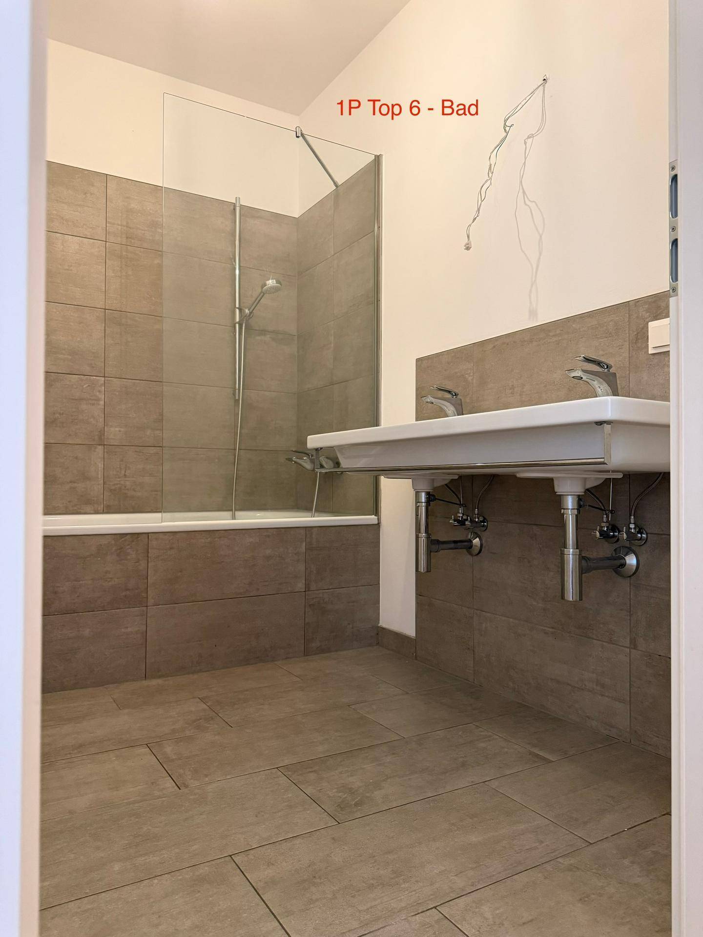 Badezimmer mit Badewanne, Duschabtrennung und Doppelwaschbecken in neutralen Grautönen.