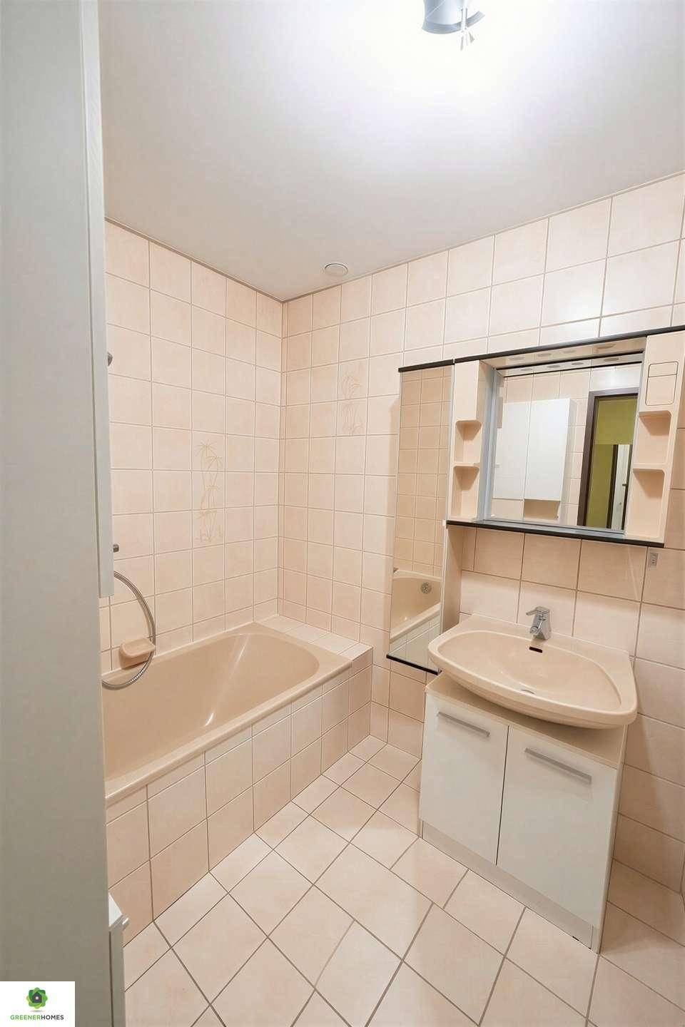 Badezimmer mit beigefarbenen Fliesen, Badewanne und Waschbecken mit Spiegelschrank.