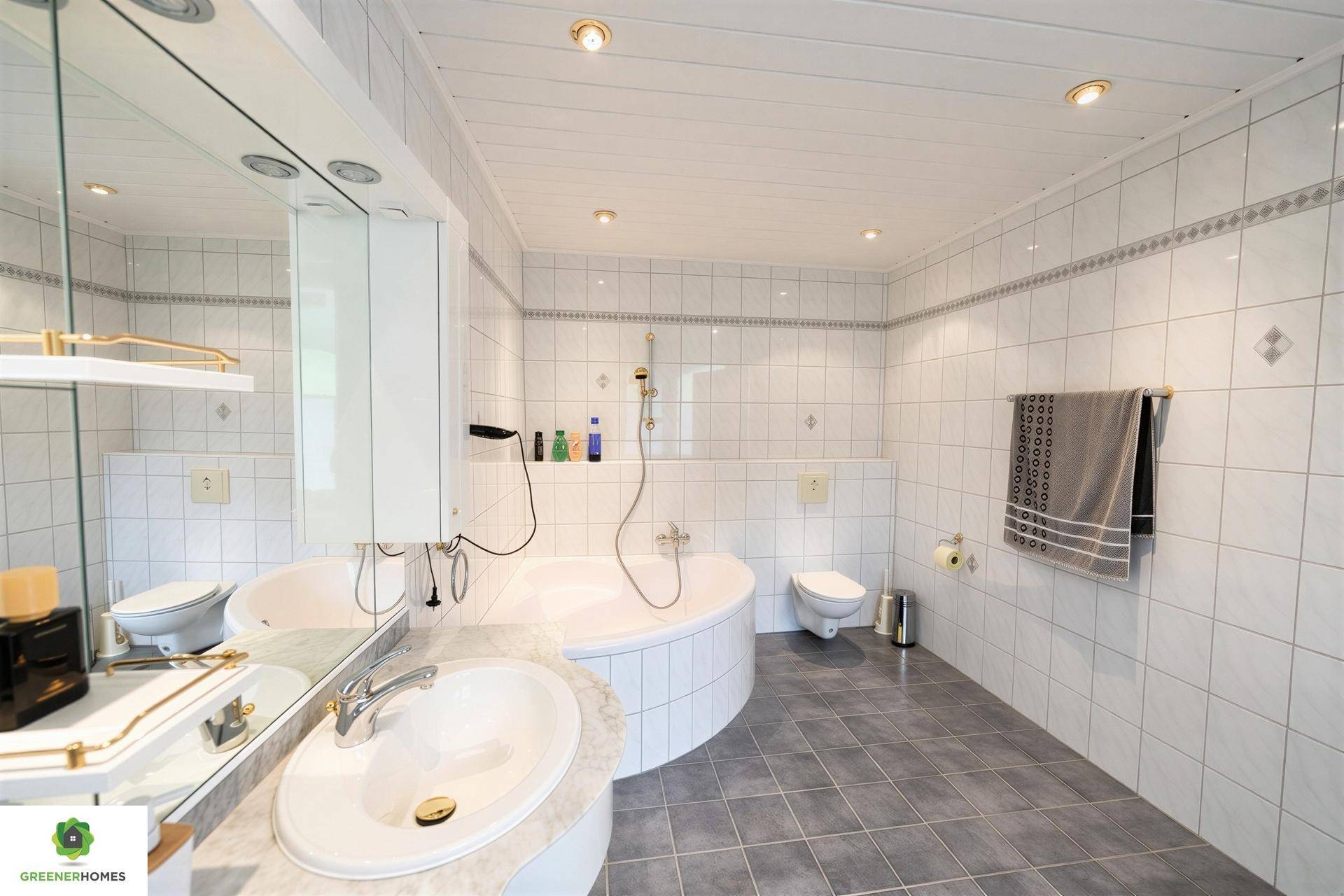 Geräumiges Badezimmer mit weißen Fliesen, Eckbadewanne und integriertem Waschtisch.