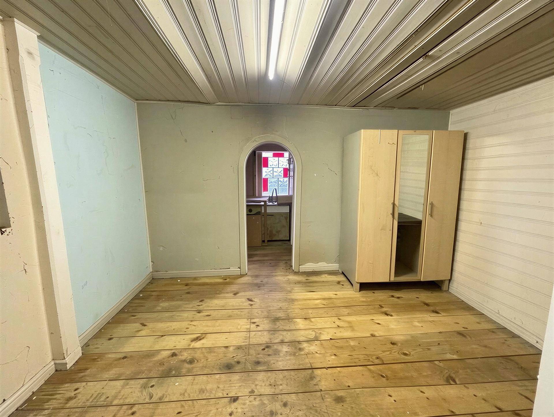 Leerer Raum mit Holzdielenboden, hellblauen Wänden und einem Durchgang zu einem weiteren Zimmer.