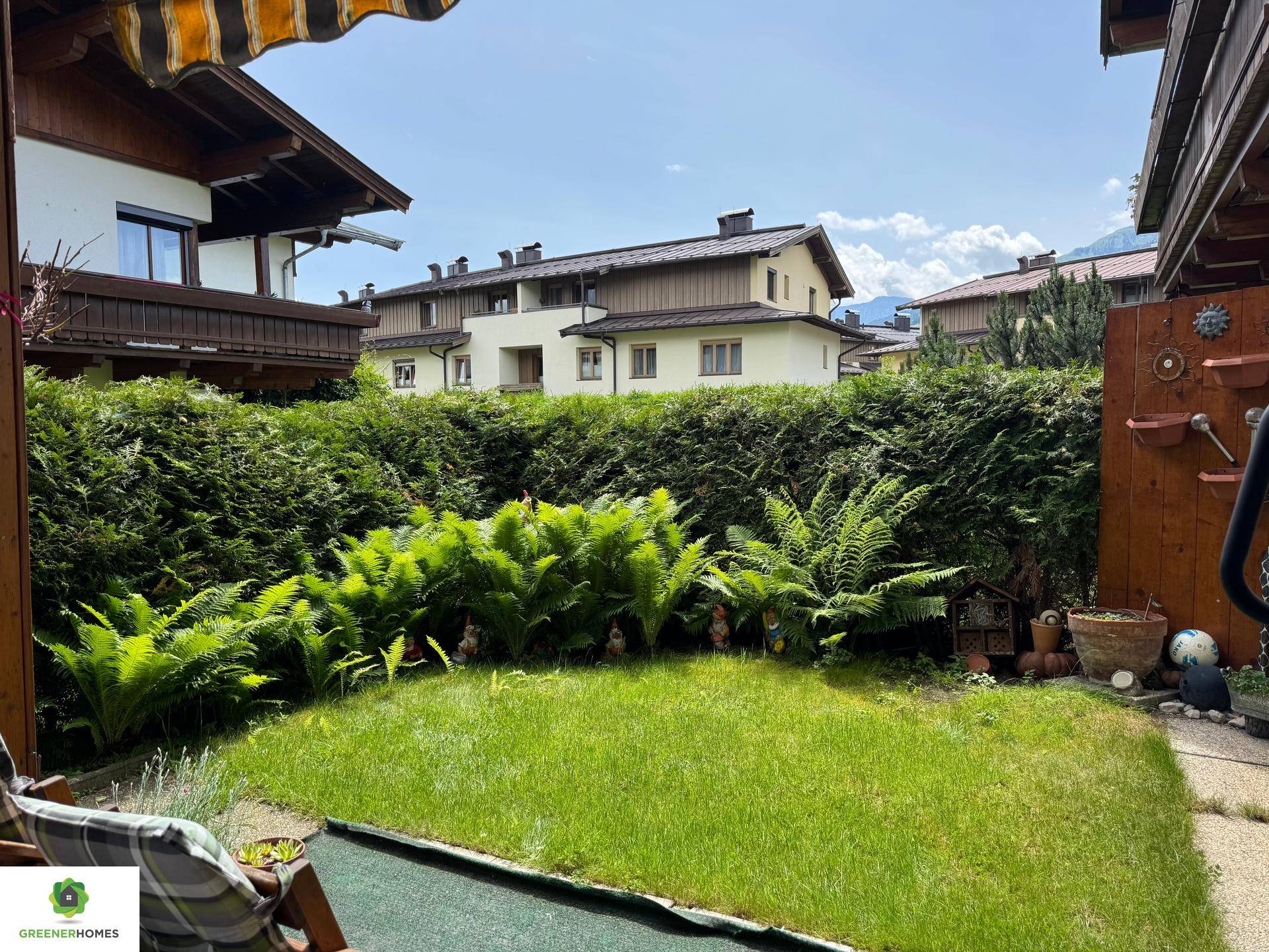 Gepflegter Gartenbereich mit Rasenfläche, hohen Hecken und Blick auf die umliegenden Häuser.