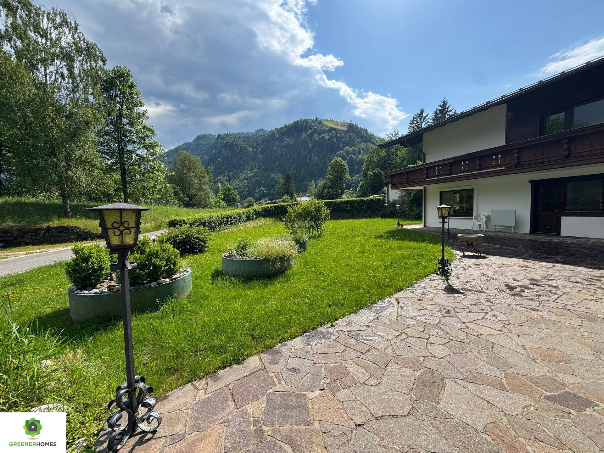 Großer Gartenbereich mit Rasenfläche, gepflastertem Weg und Blick auf die Berge.