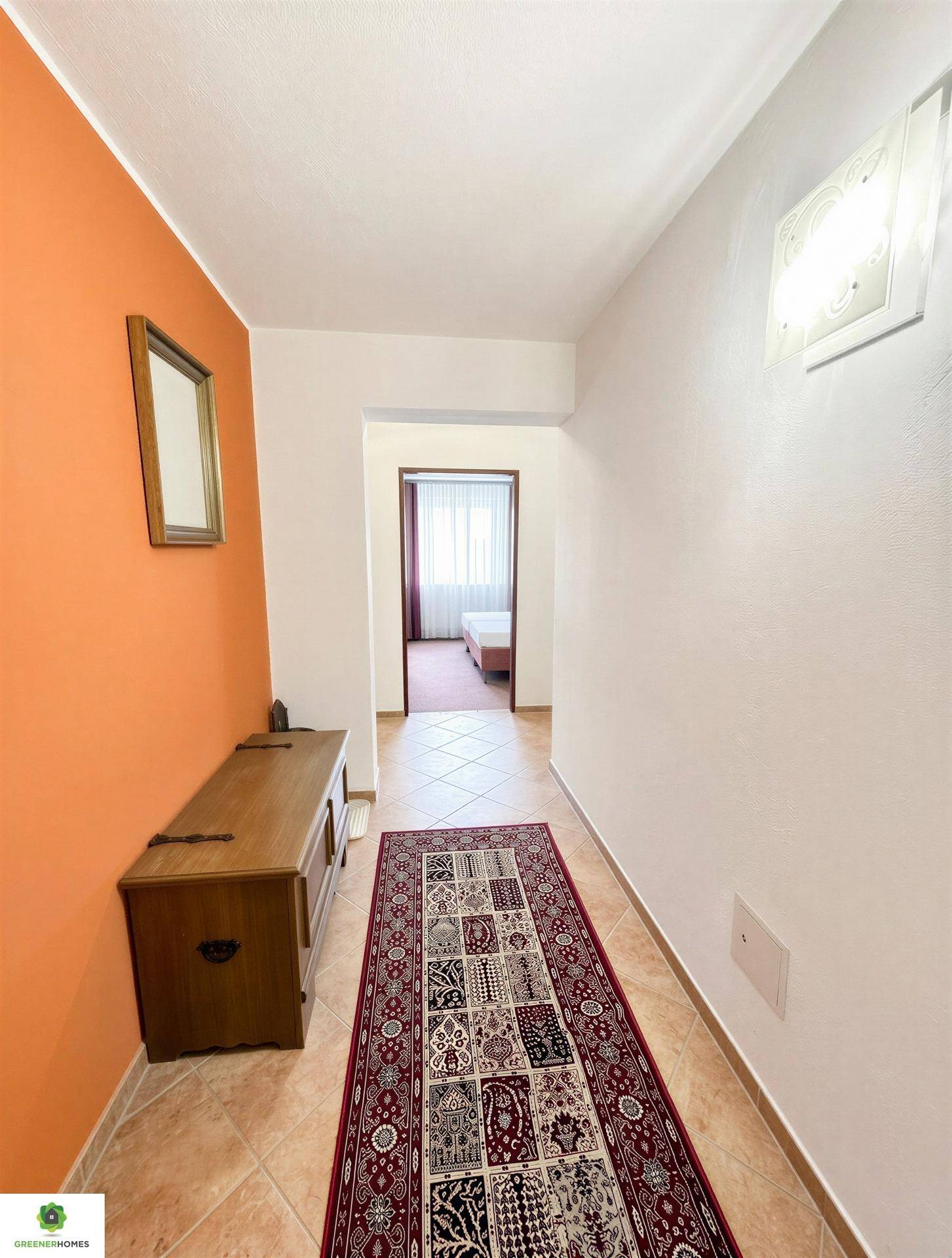 Heller Flur mit orangefarbener Akzentwand, Fliesenboden und einem traditionellen Teppichläufer.