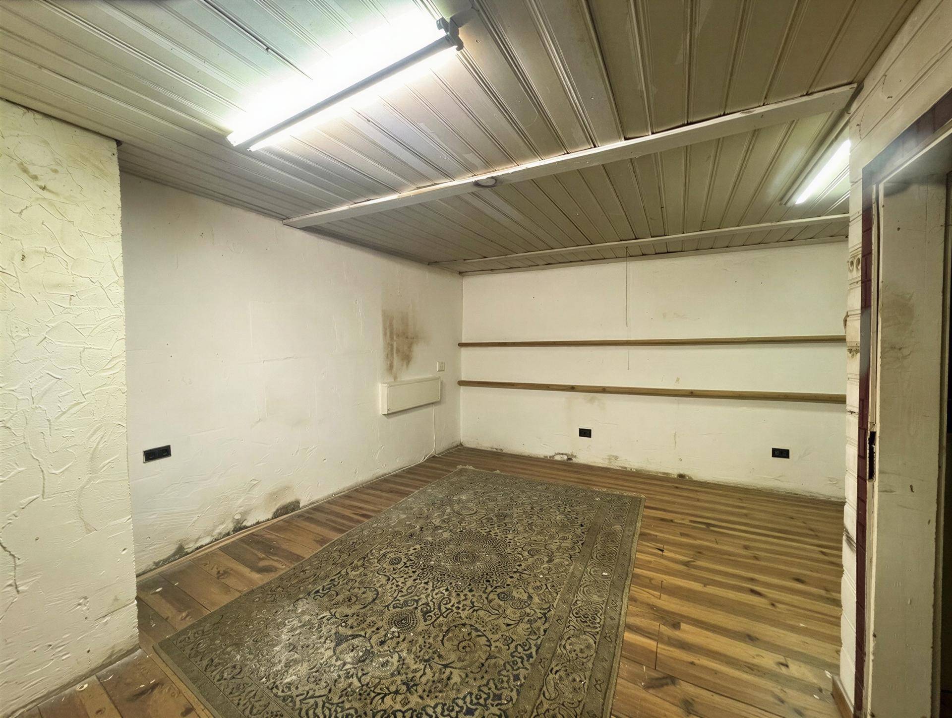 Leerer Raum mit Holzdielenboden, weiß gestrichenen Wänden und einer Deckenverkleidung.