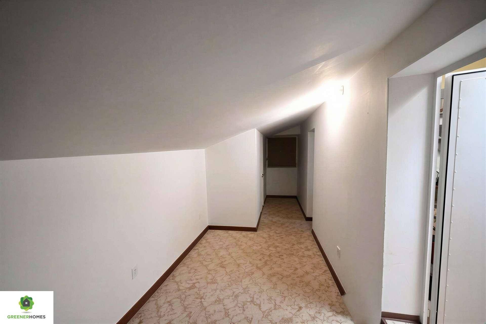 Langer, schmaler Raum im Dachgeschoss mit schrägen Wänden und Teppichboden.