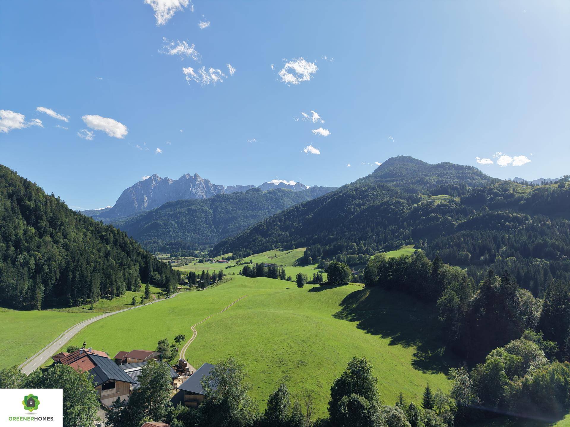 Malerische Luftaufnahme eines grünen Tals mit Bergen, Wäldern und vereinzelten Häusern.