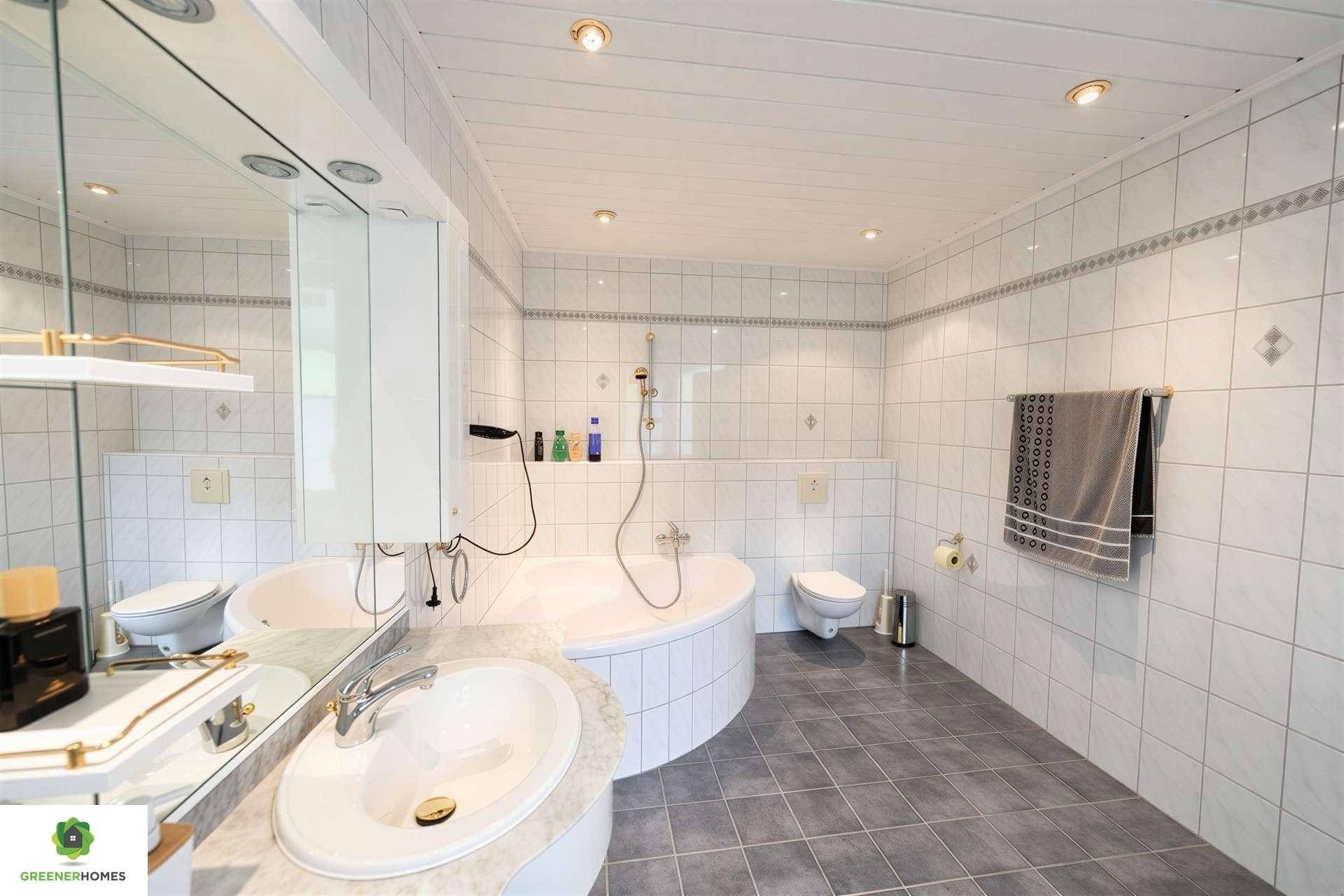 Helles Badezimmer mit weißen Fliesen, Eckbadewanne und Einzelwaschbecken.