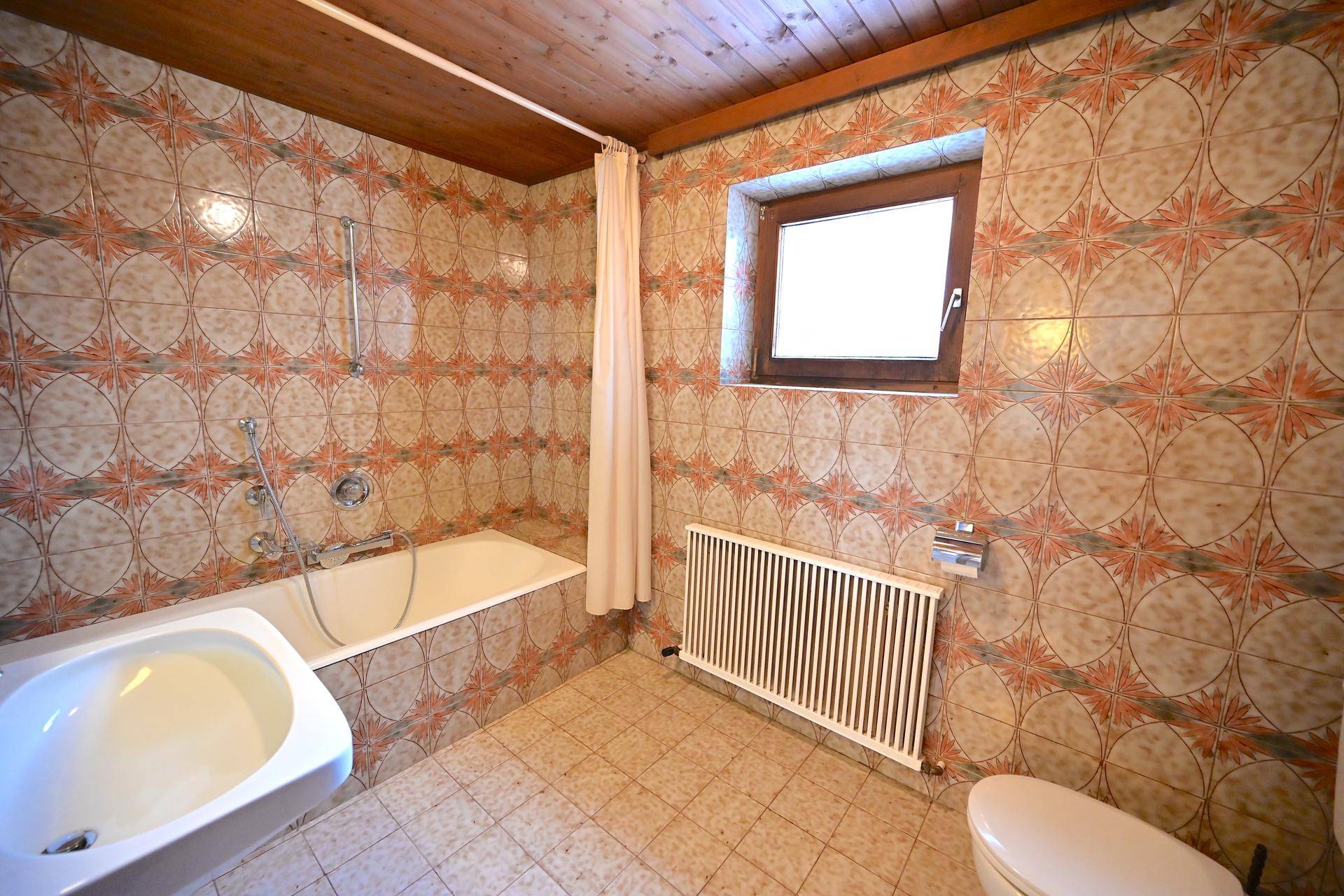 Badezimmer mit Badewanne, WC, Fenster und gemusterten Fliesen im traditionellen Stil.