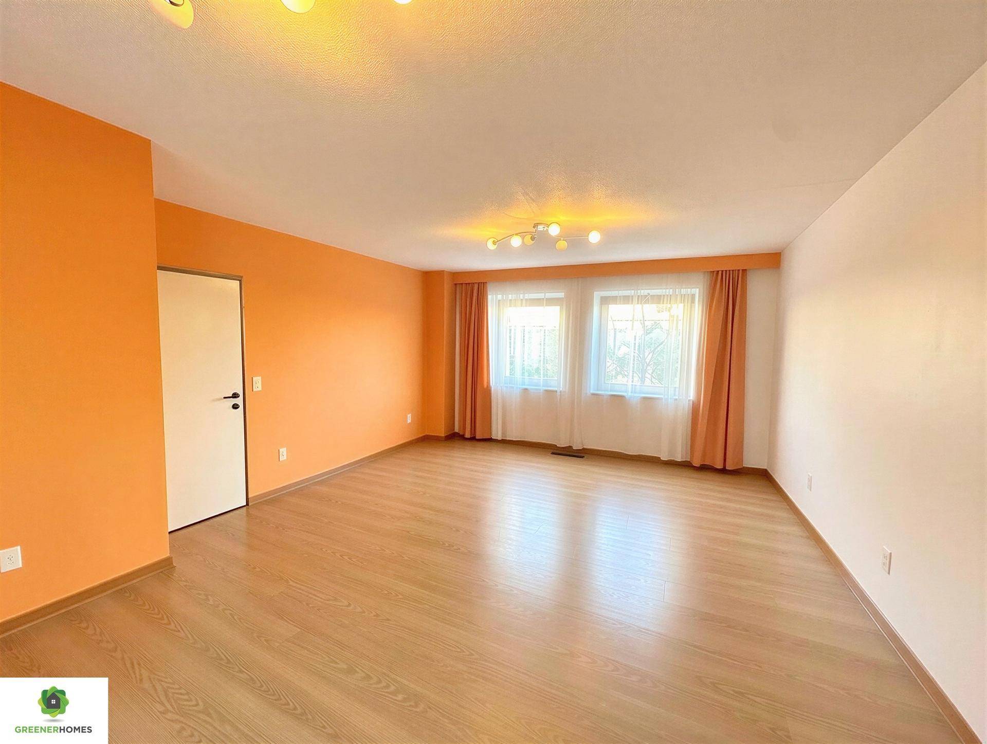 Heller, leerer Raum mit orangefarbenen Wänden, Laminatboden und zwei großen Fenstern.