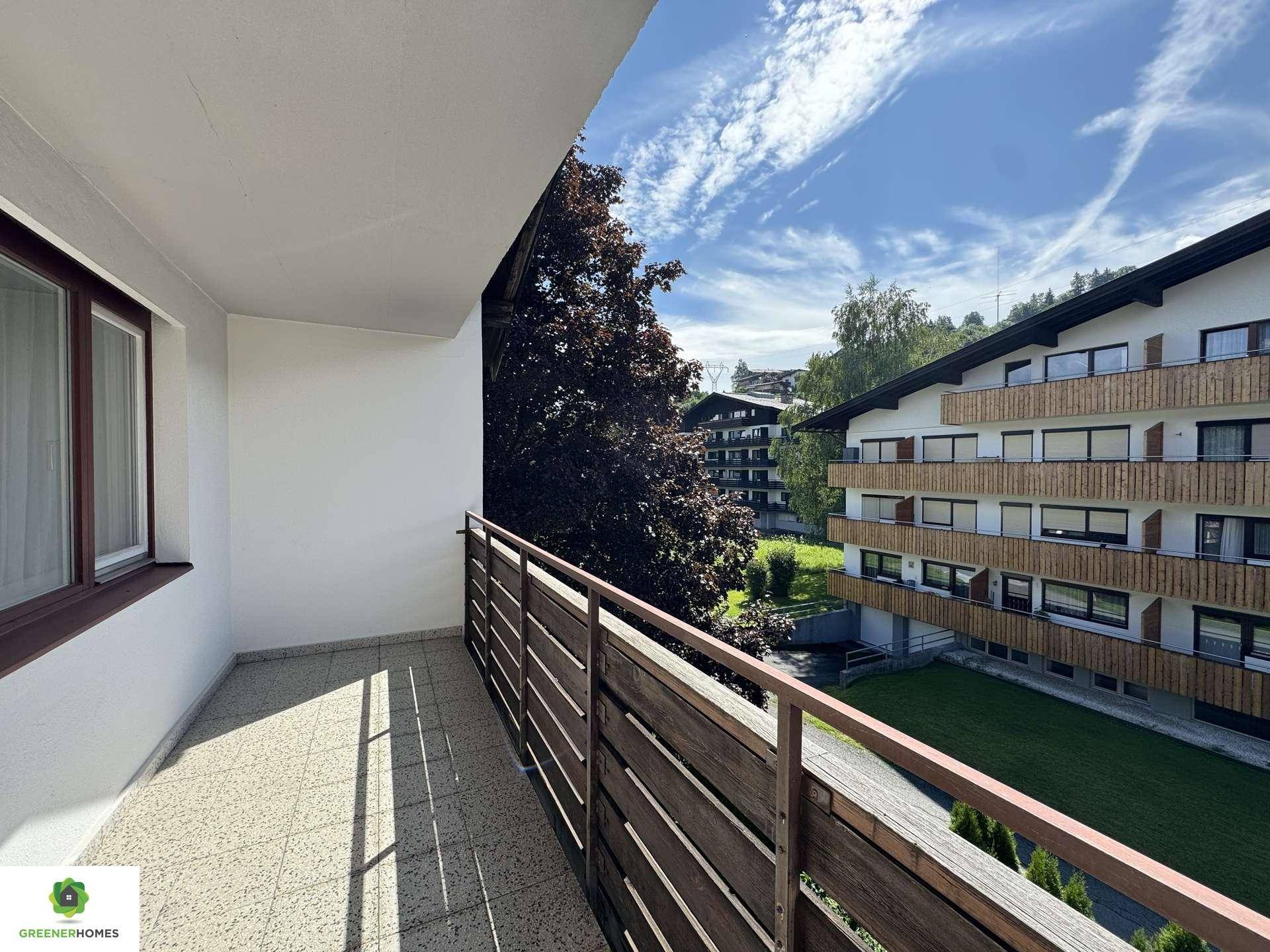 Balkon mit Fliesenboden und Holzgeländer, bietet einen Blick auf den grünen Innenhof und benachbarte Gebäude.