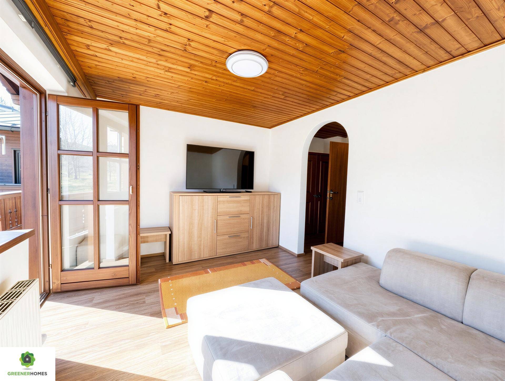 Helles Wohnzimmer mit Holzbalkendecke, Sofa und Zugang zu einem Balkon.