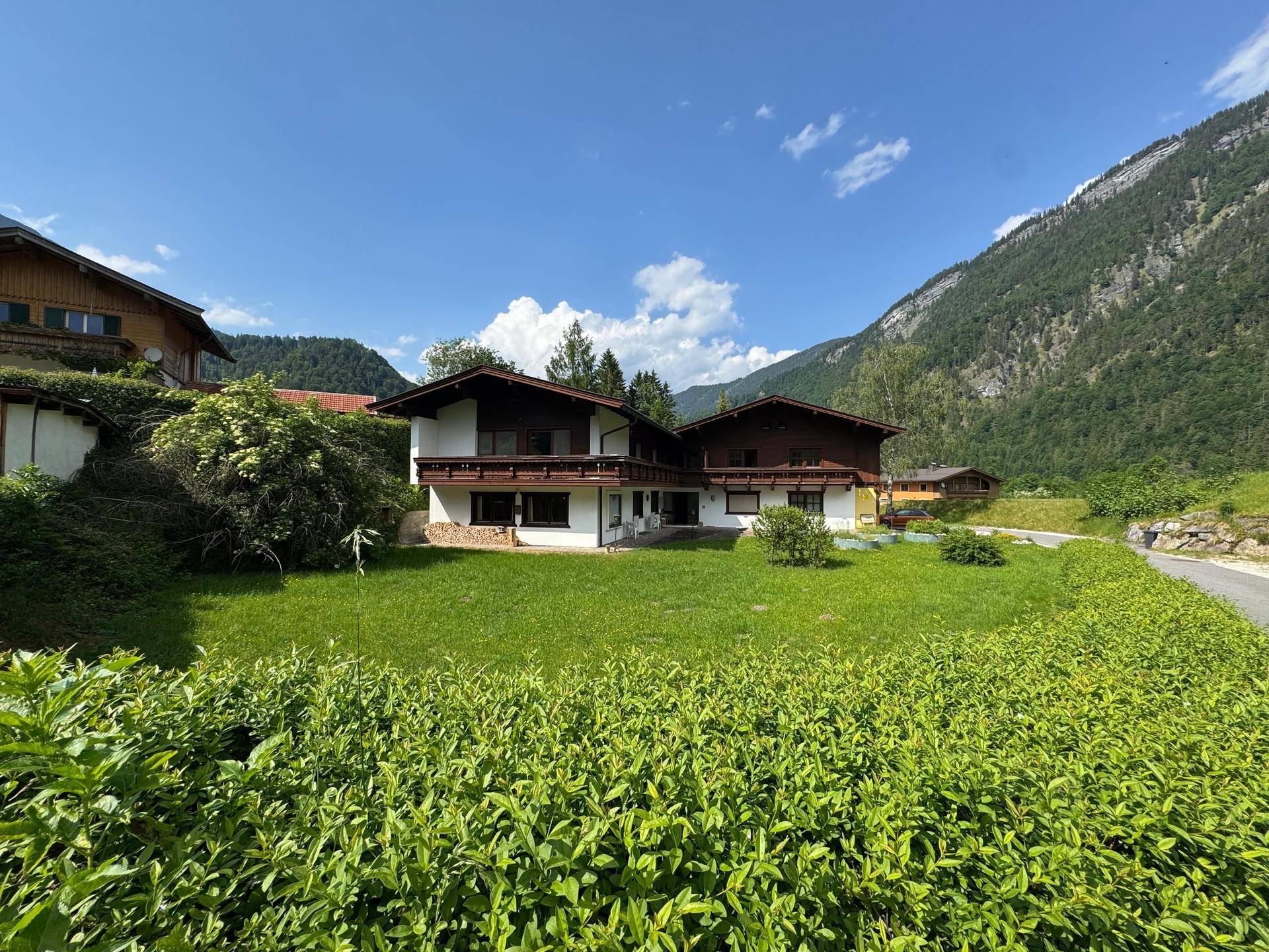 Traditionelles Haus mit weißer Fassade, Holzbalkonen und grüner Umgebung.