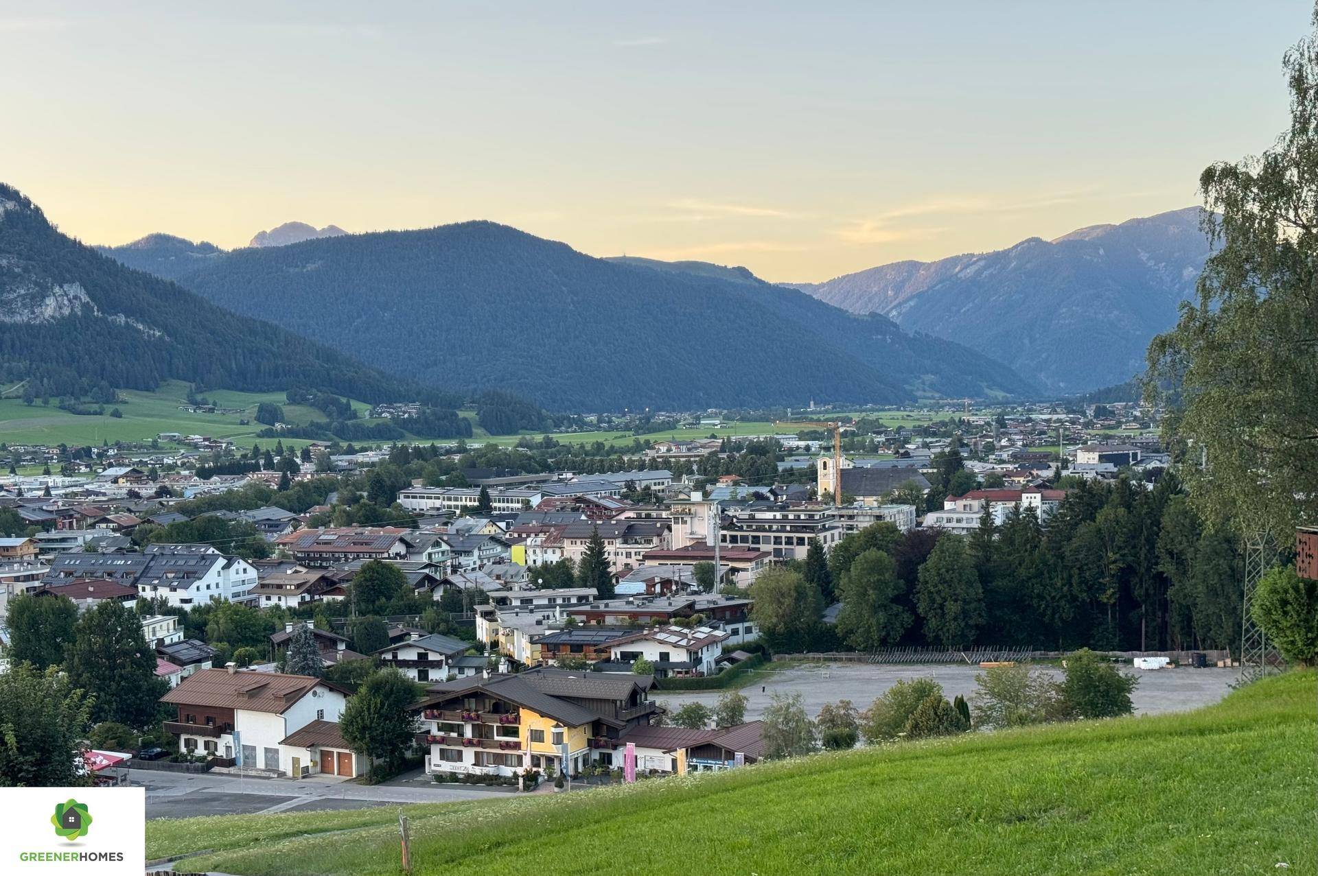 Panoramablick auf eine malerische Stadt im Tal, umgeben von Bergen und grünen Hügeln.