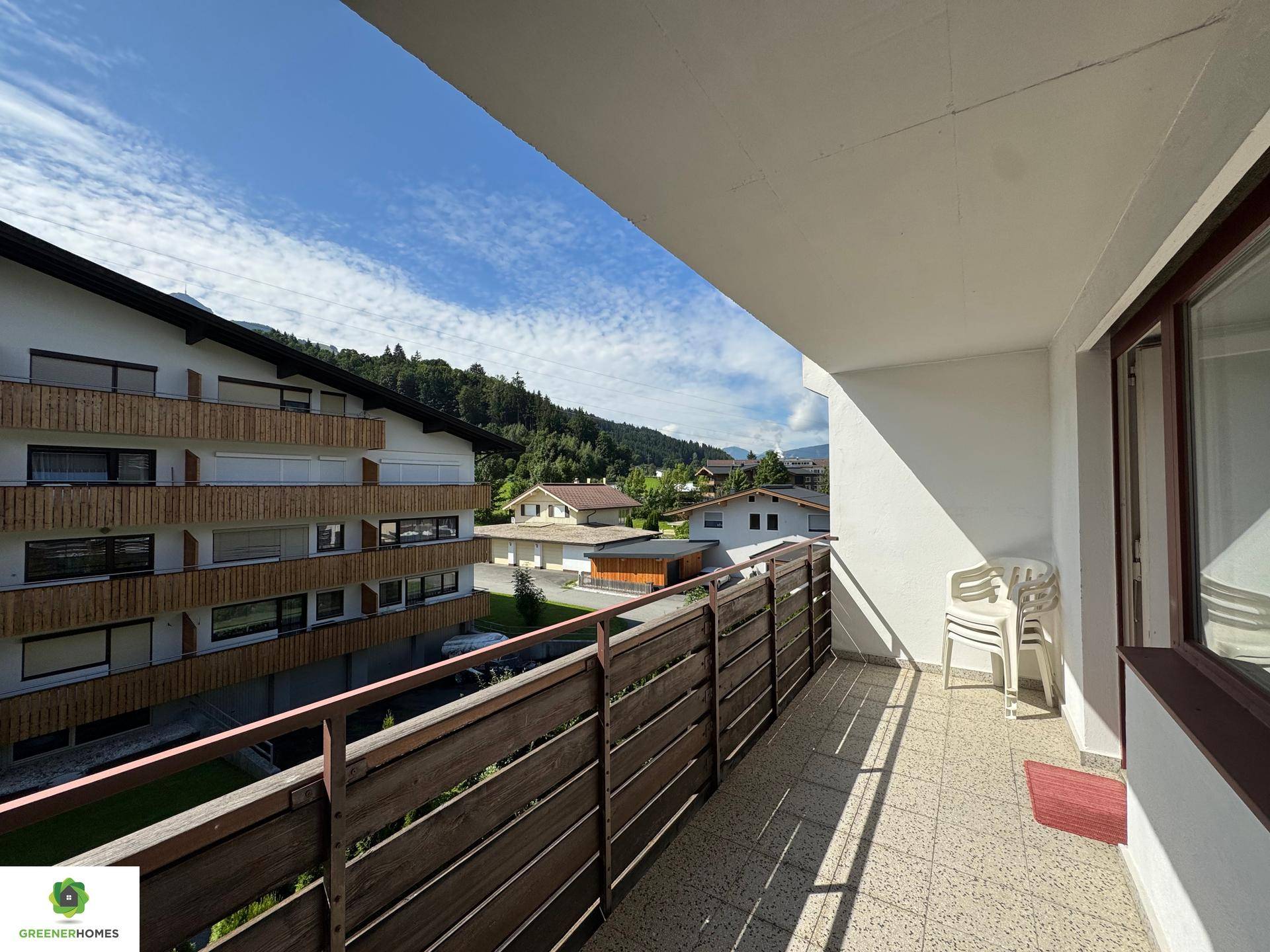 Sonniger Balkon mit einfacher Bestuhlung, Fliesenboden und weitem Blick auf die bergige Umgebung.