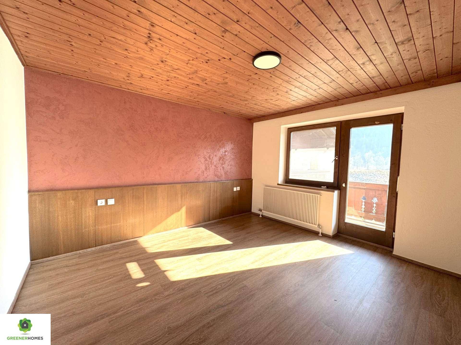 Geräumiges Zimmer mit Holzbalkendecke, Laminatboden und einer strukturierten Akzentwand.