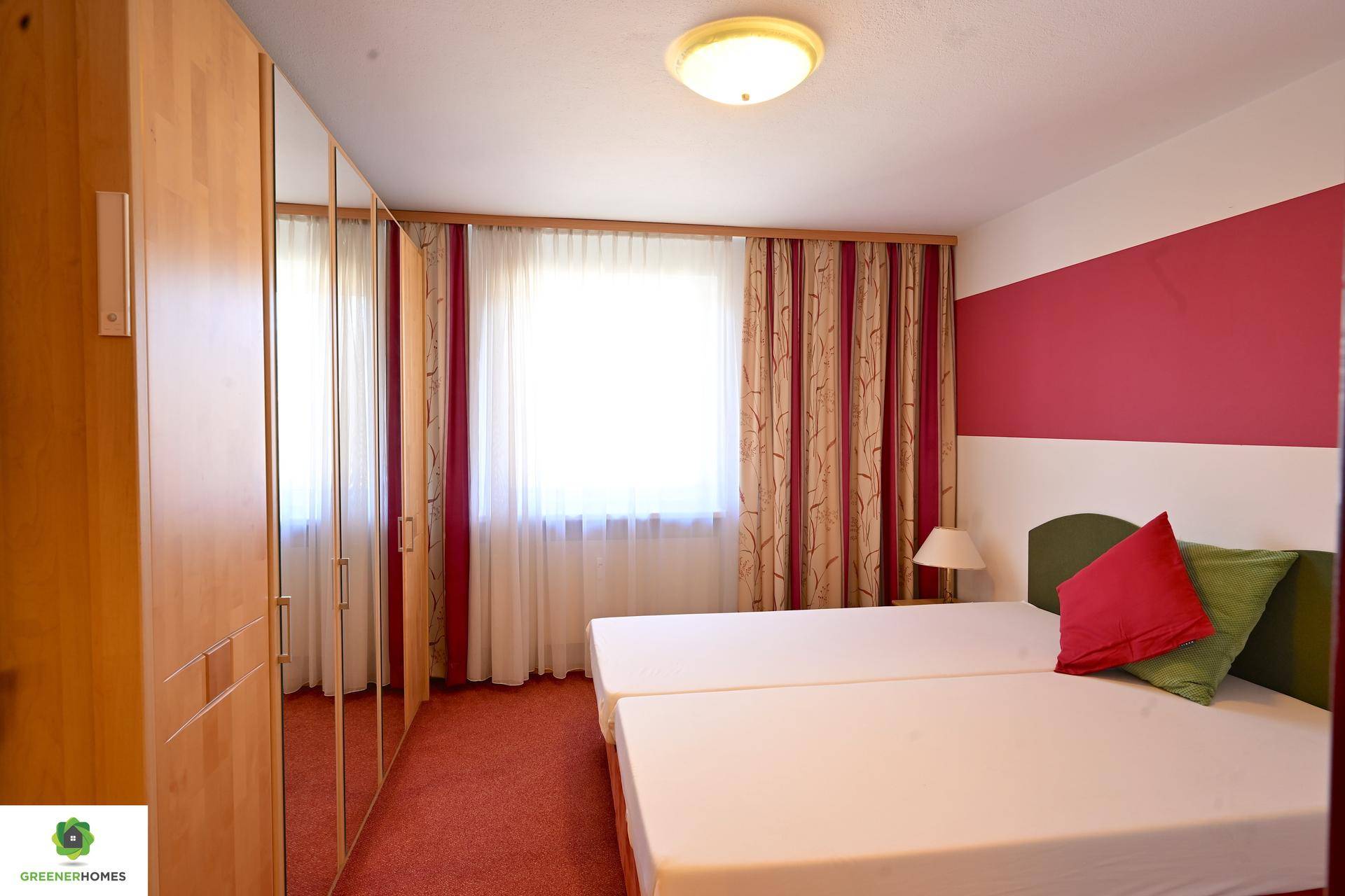 Schlafzimmer mit zwei Einzelbetten, rotem Teppichboden und einem großen Kleiderschrank mit Spiegeltüren.
