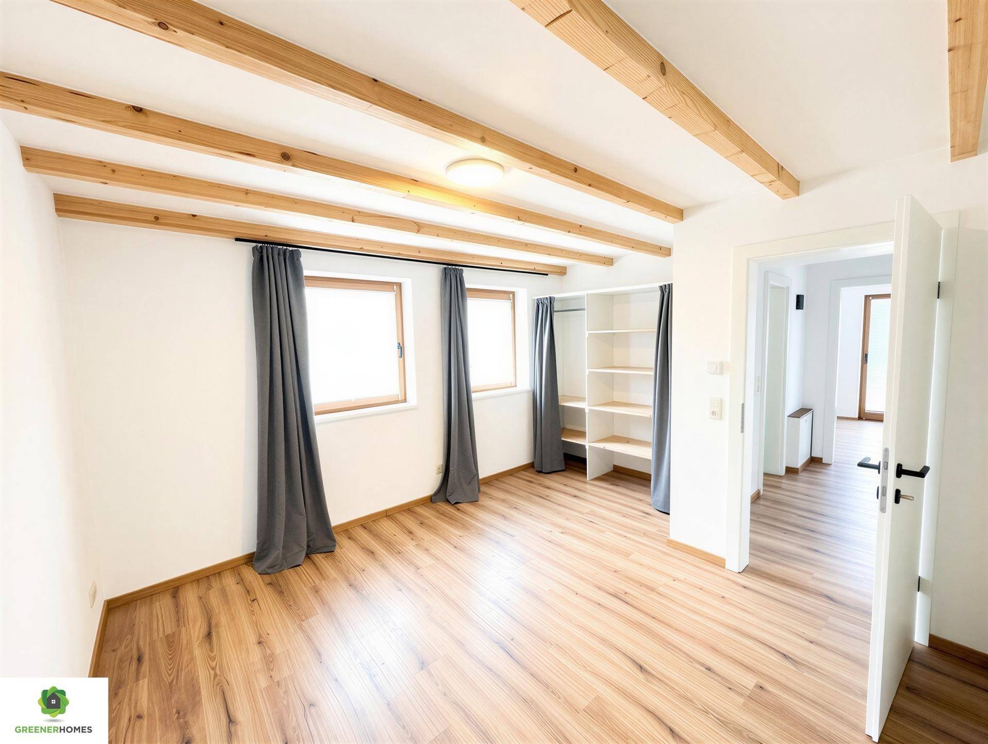 Geräumiges Schlafzimmer mit Holzbalkendecke, Laminatboden und einem offenen Kleiderschrank.