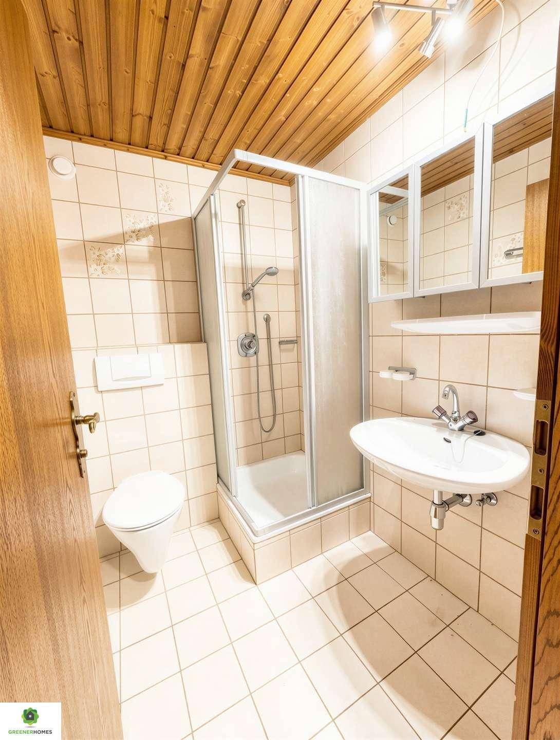 Gefliestes Badezimmer mit Duschkabine, Waschbecken, WC und Holzdecke im traditionellen Stil.