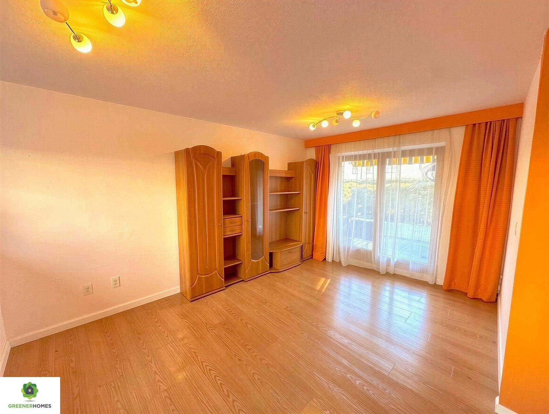 Wohnraum mit Holzmöbeln, Laminatboden und Zugang zu einem Außenbereich durch eine große Glastür.
