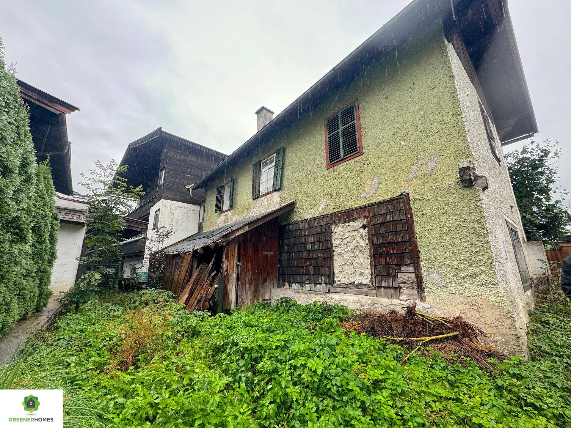 Seitenansicht eines älteren Hauses mit grüner Putzfassade und Holzanbauten.