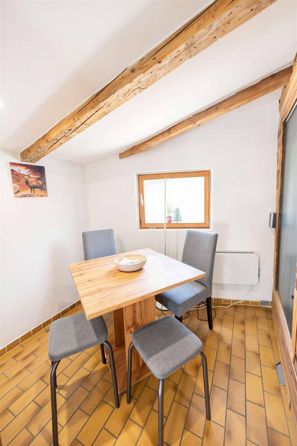 Kleiner Essbereich mit Holztisch, Stühlen und sichtbaren Deckenbalken, hell und rustikal gestaltet.
